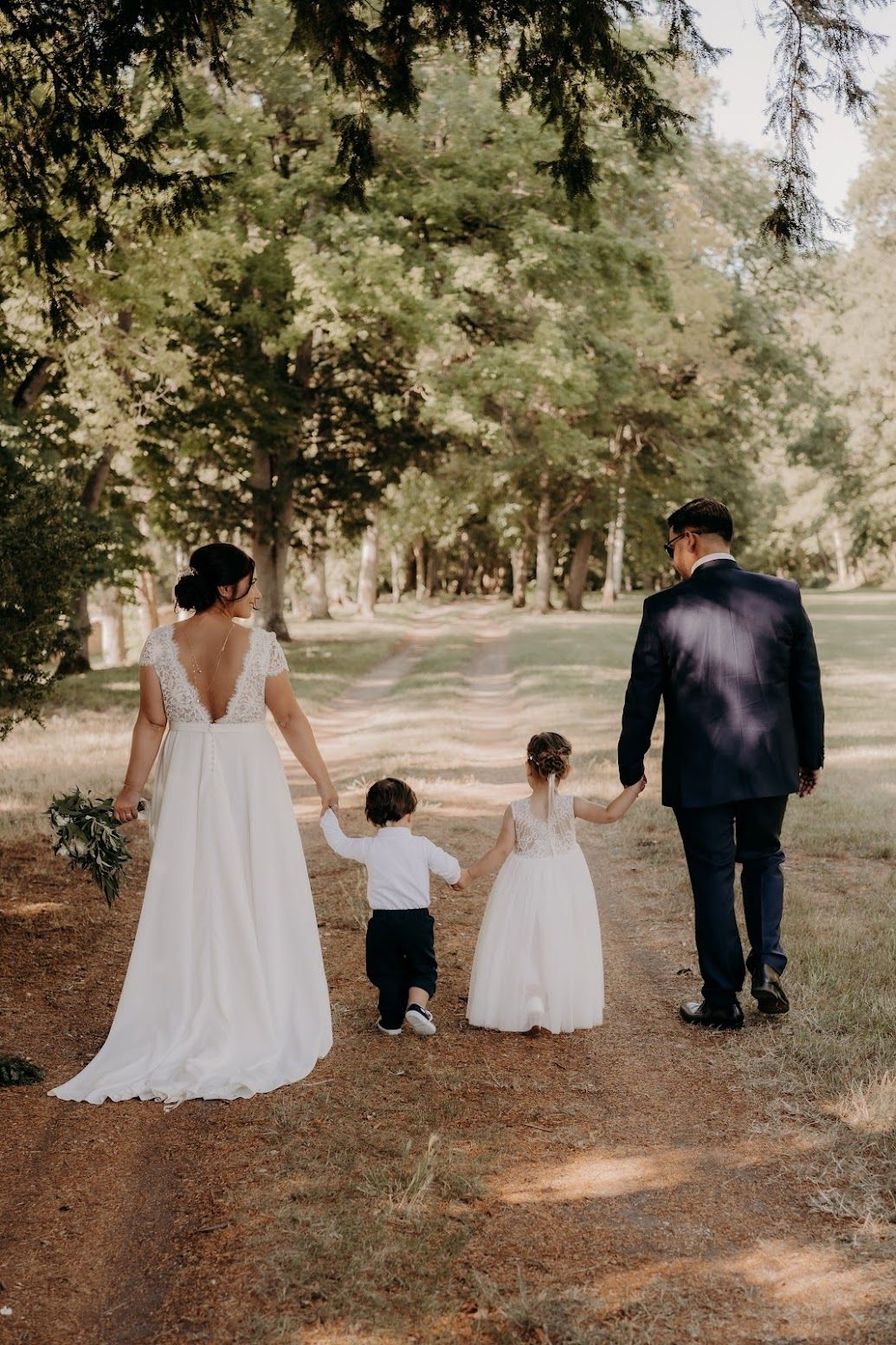 Family walking together on a tree-lined path in formal attire.