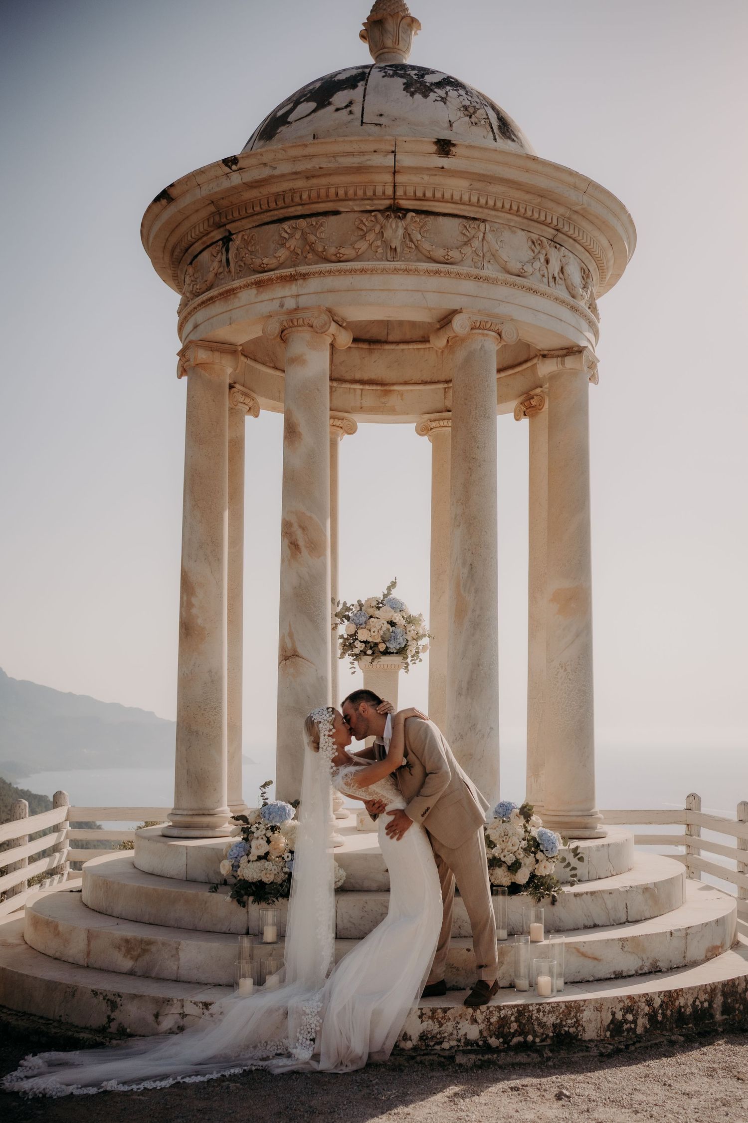Romantic wedding moment in classical stone gazebo overlooking coastal view.