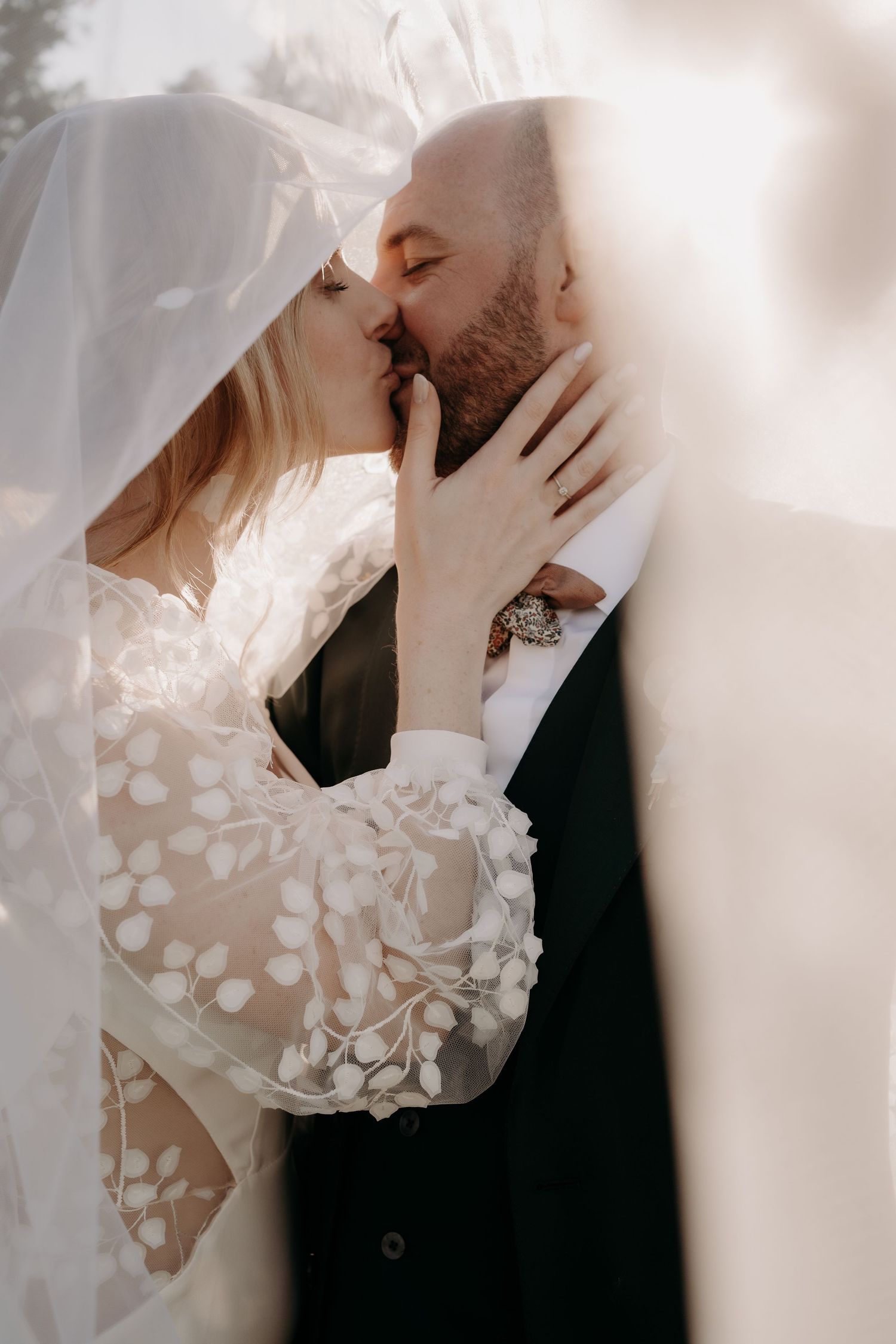 Romantic wedding couple sharing an intimate moment under a delicate floral veil in soft lighting.