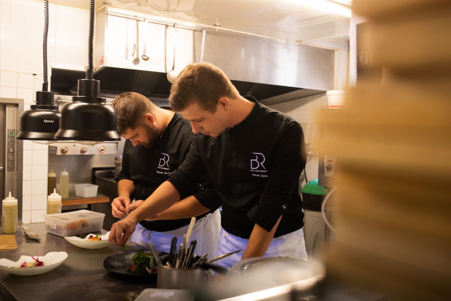 Professional chefs working in a commercial kitchen with stainless steel equipment.