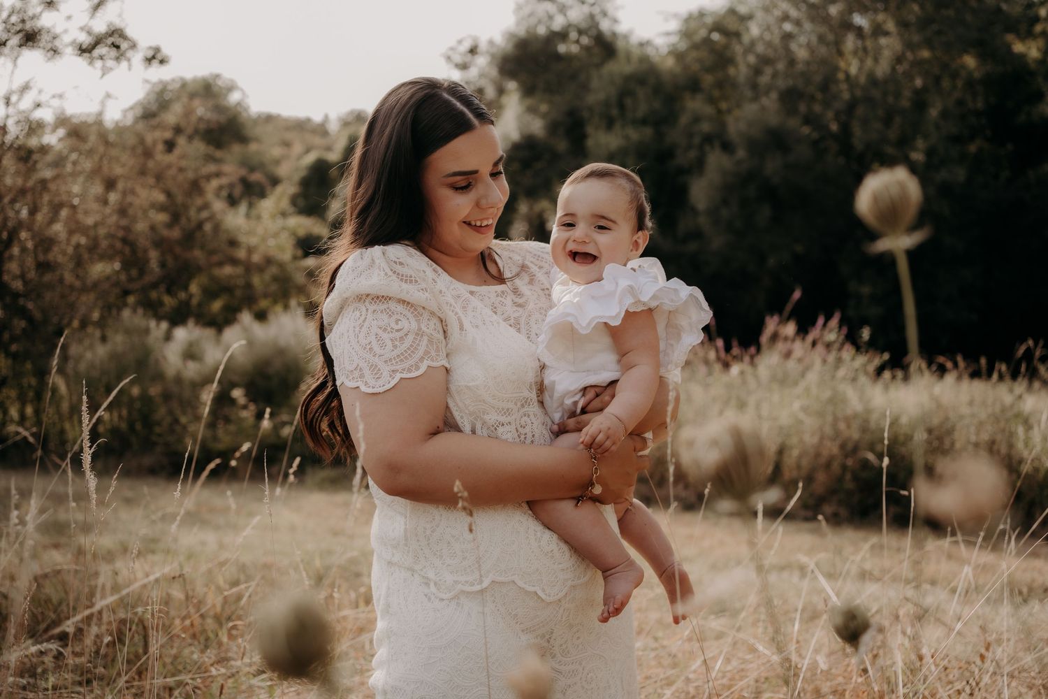 A family poses together in a golden field during sunset wearing coordinated white outfits.