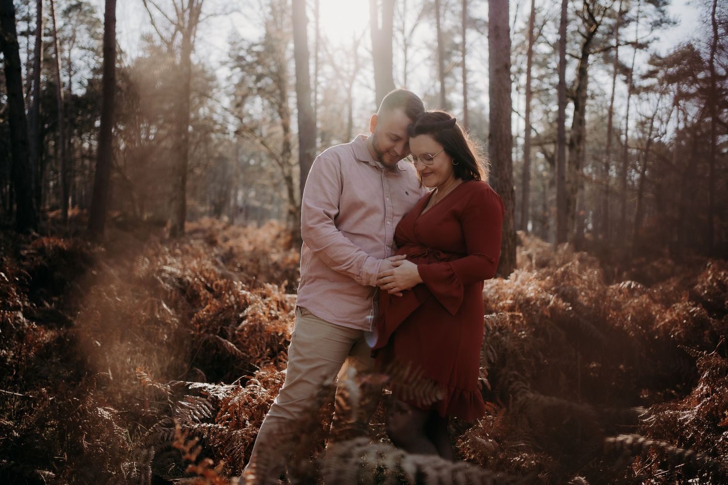 Romantic forest engagement session with sunlight filtering through trees.