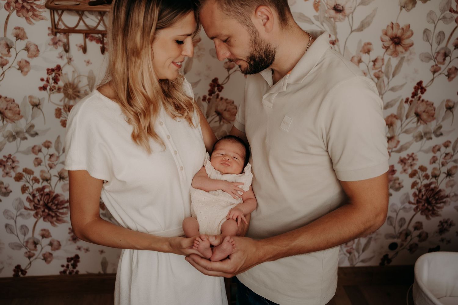 Lifestyle newborn session with floral wallpaper background in soft lighting.