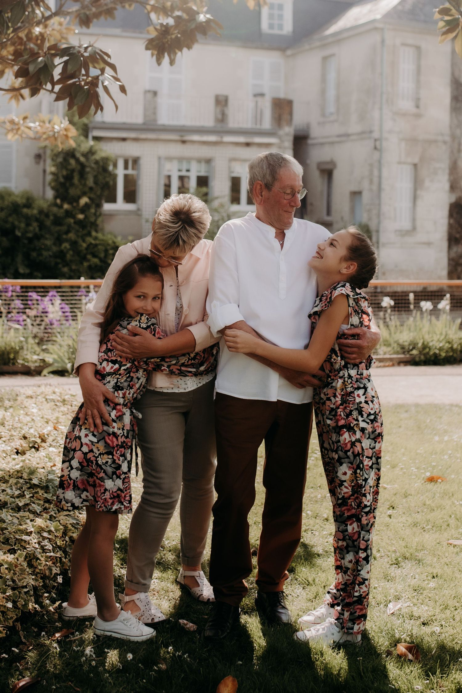 Family sharing a joyful embrace in front of a grand country house with blooming garden.