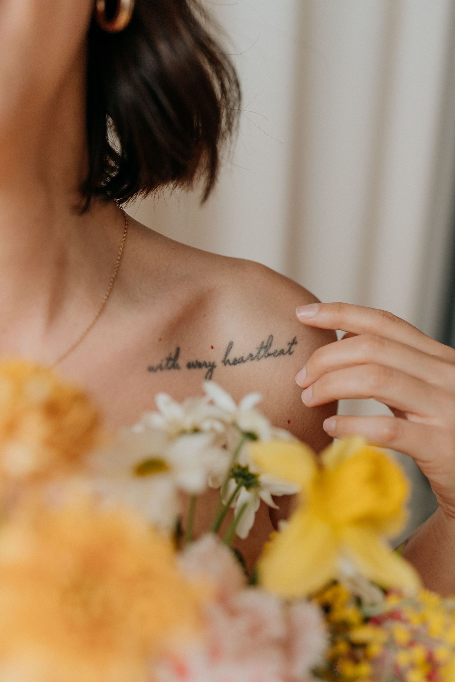 Close-up of delicate script tattoo on shoulder with flowers in soft focus.