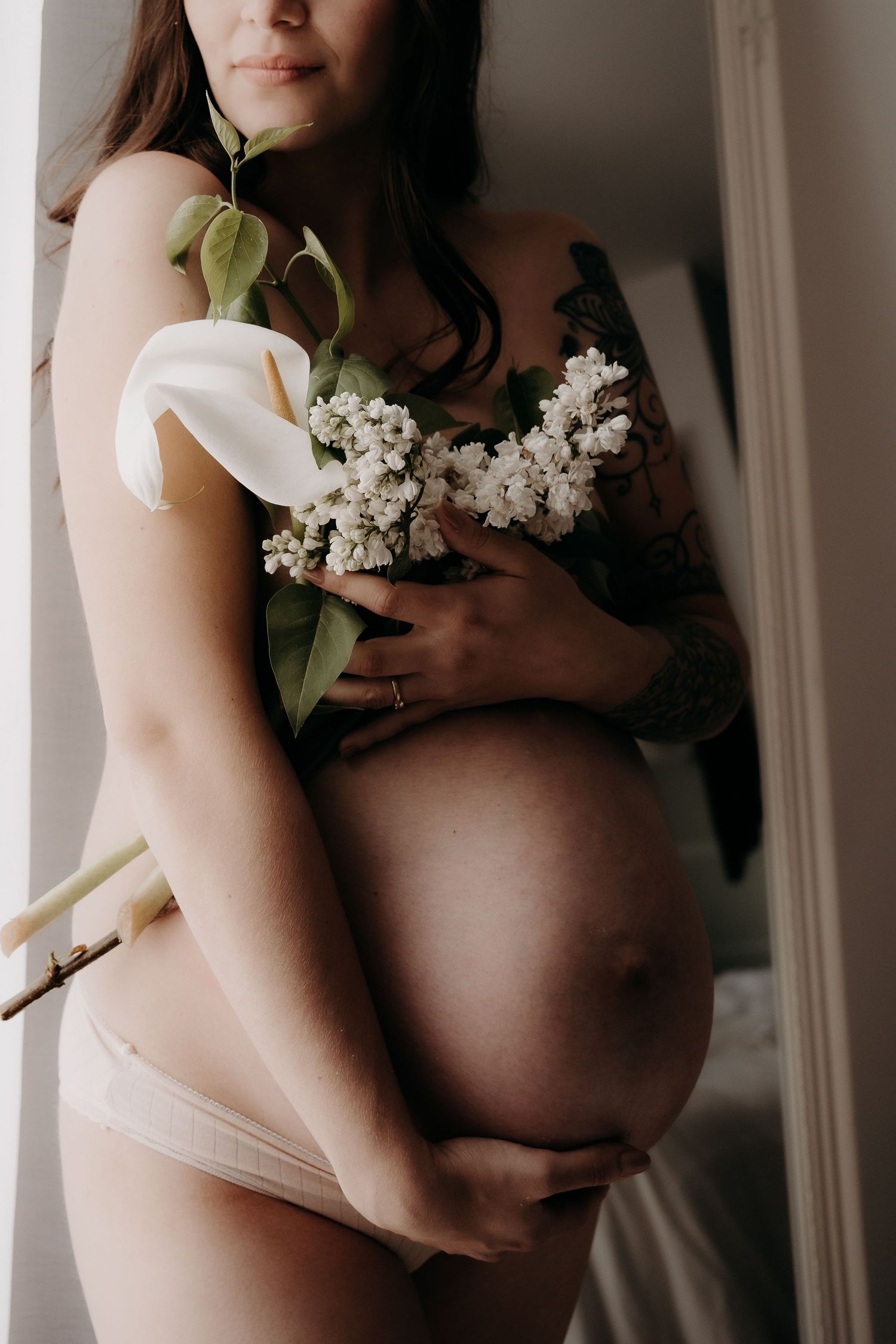 Artistic maternity photo with white calla lily and lilac flowers.