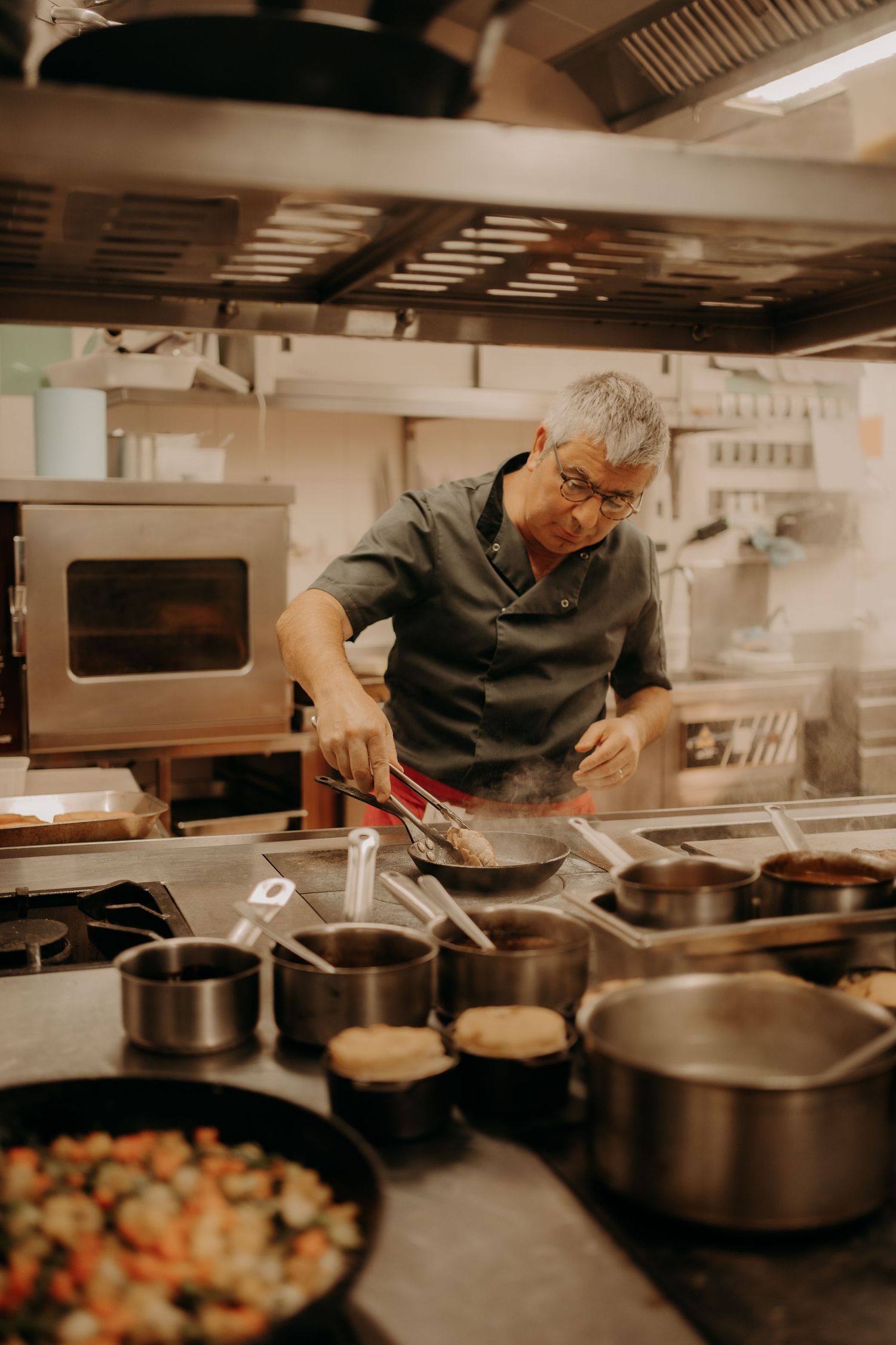 Chefs preparing food at multiple cooking stations in a professional restaurant kitchen.
