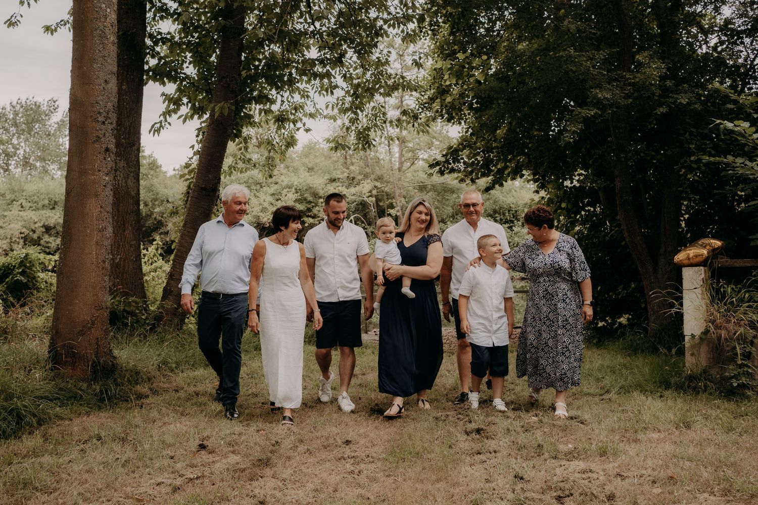 Group of people walking together on grassy path through wooded area on sunny day.