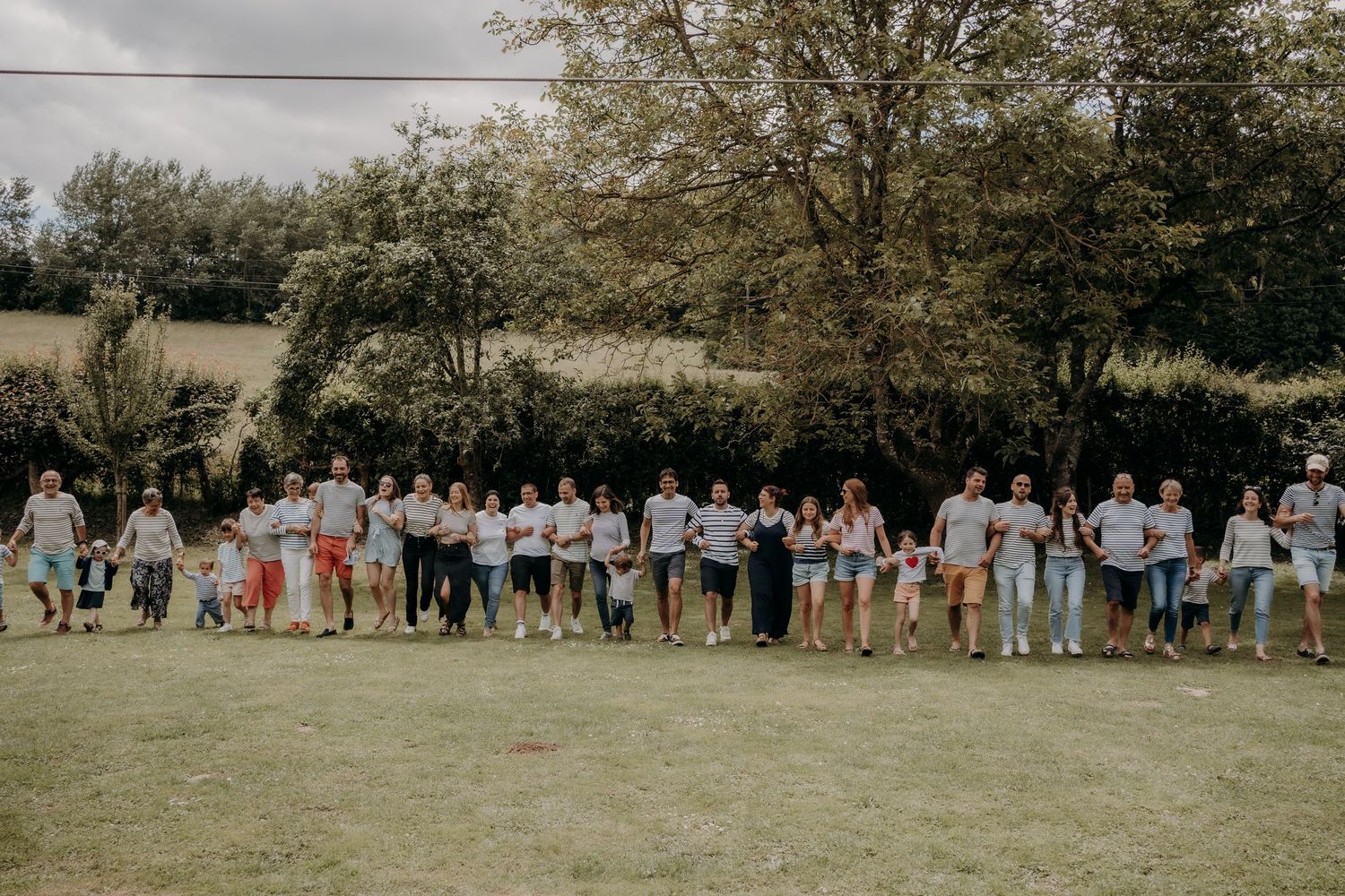 Large group photo of wedding guests lined up outdoors in casual summer attire.