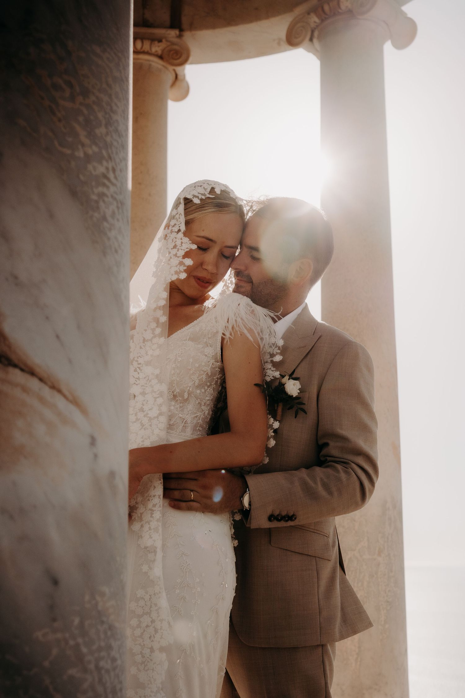 Tender wedding moment photographed between classical stone pillars.