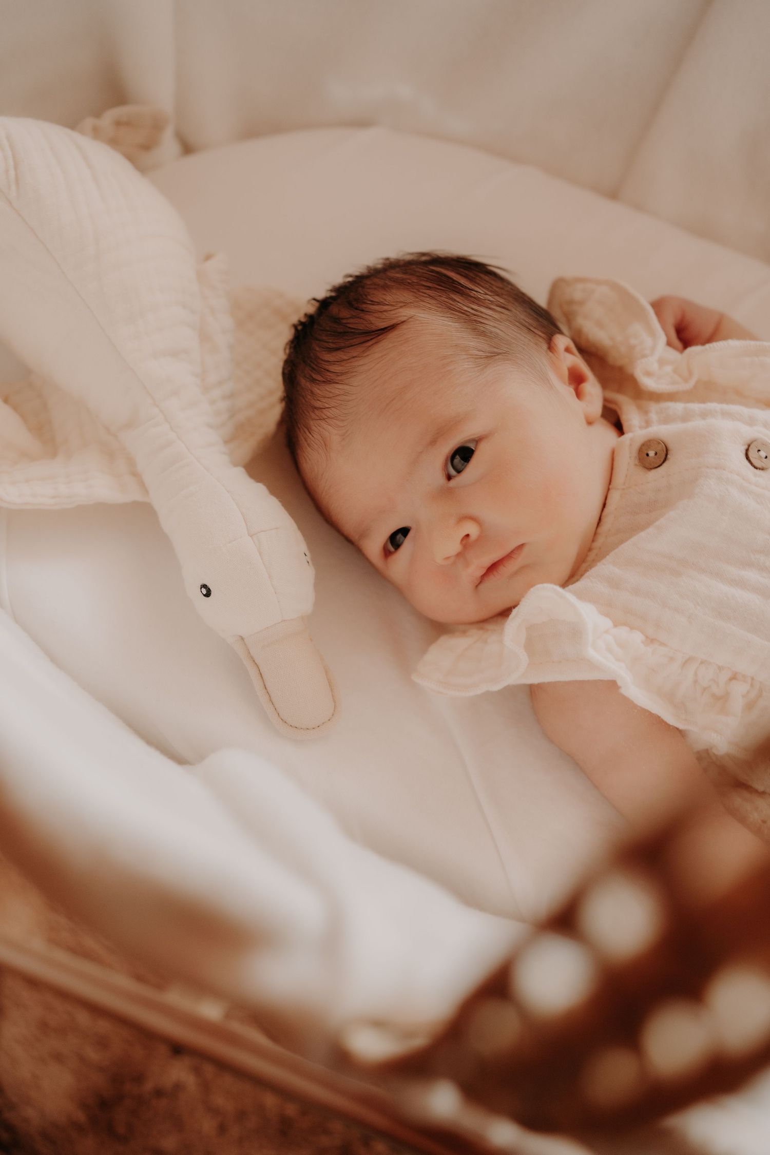 Baby in cream colored outfit lying next to stuffed bunny toy.