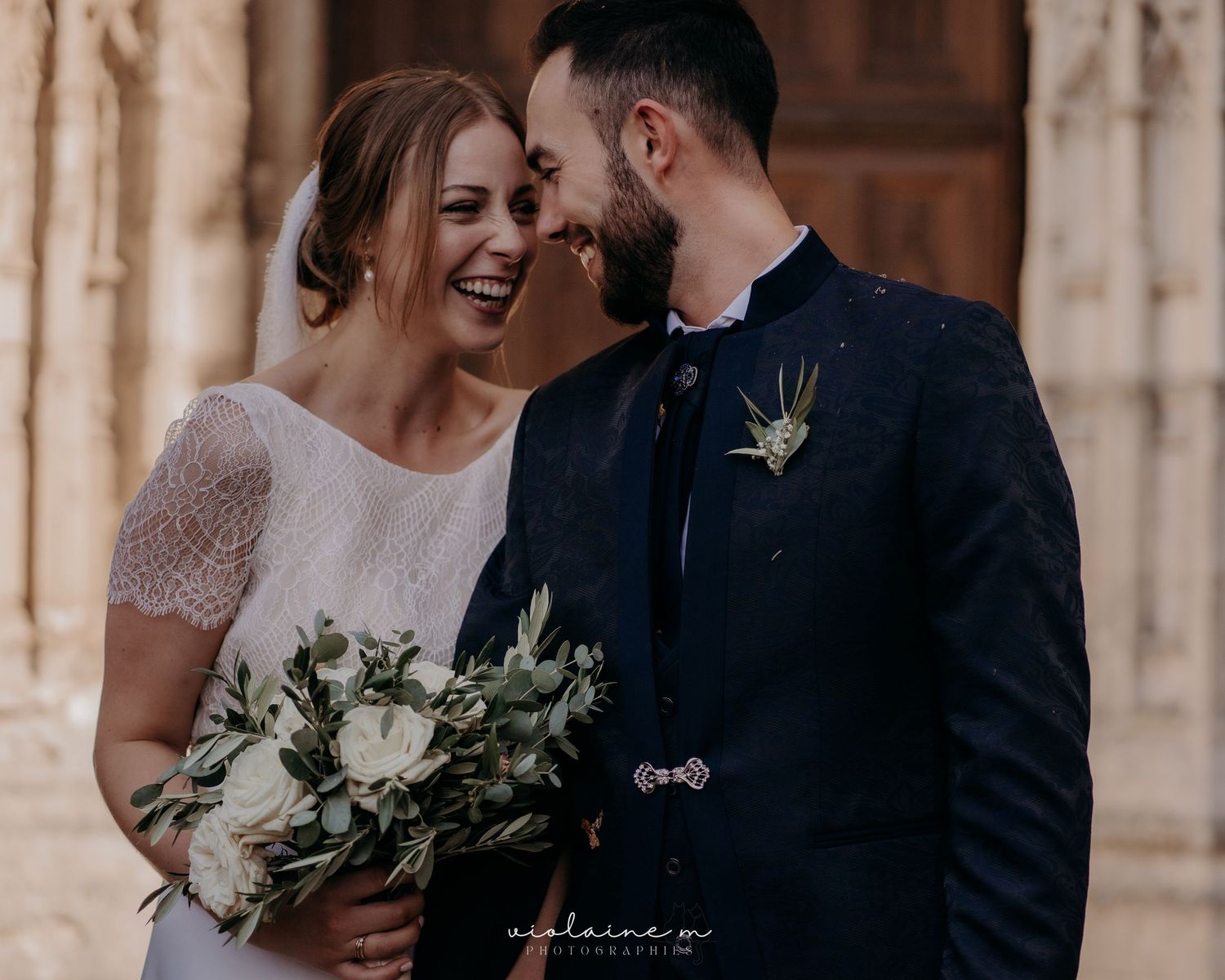 Elegant wedding couple shares joyful moment against stone architecture.