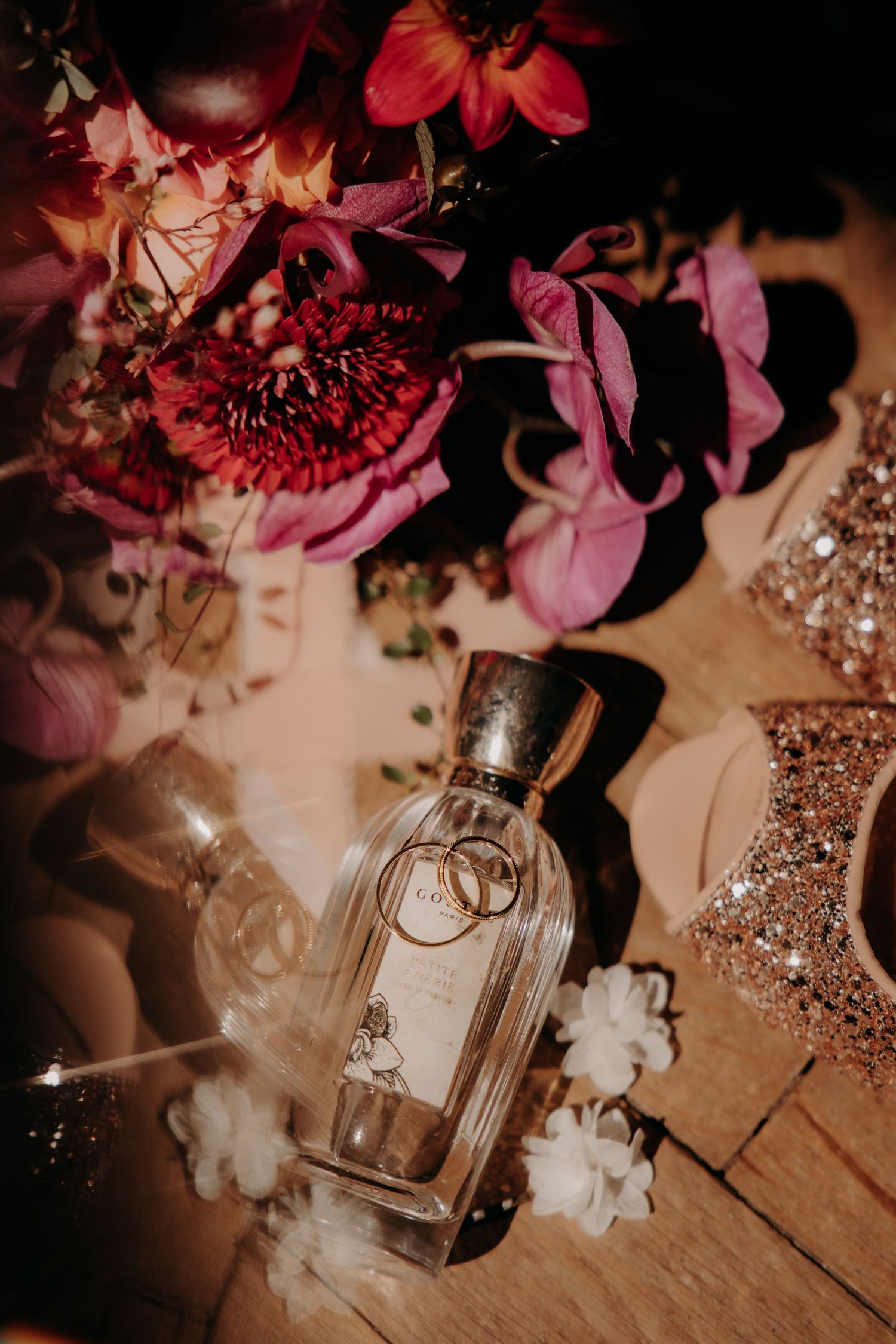 Wedding details with pink flowers and crystal perfume bottles on rustic wooden surface.