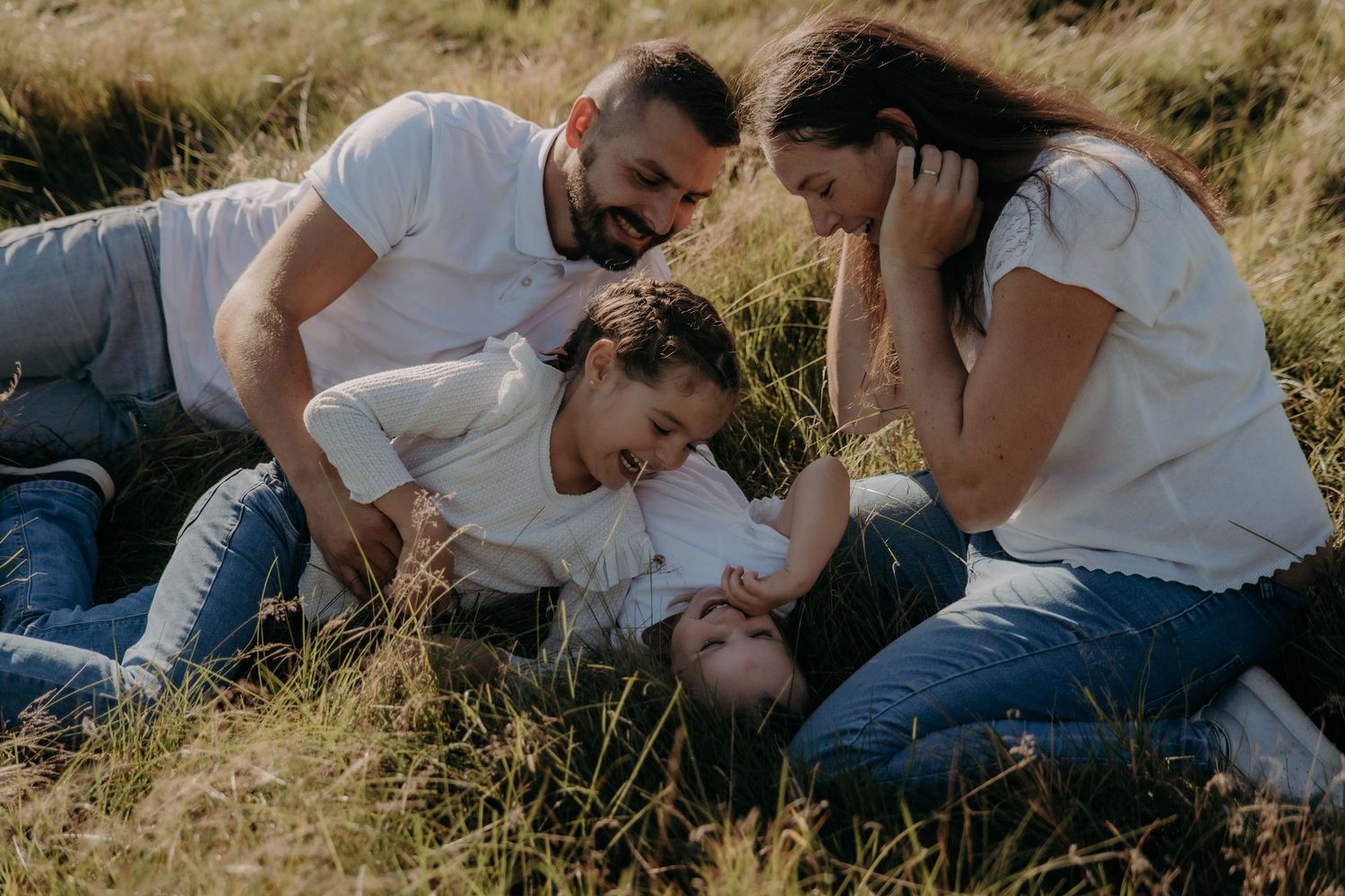 Candid lifestyle photography of people relaxing together in tall grass during golden hour.