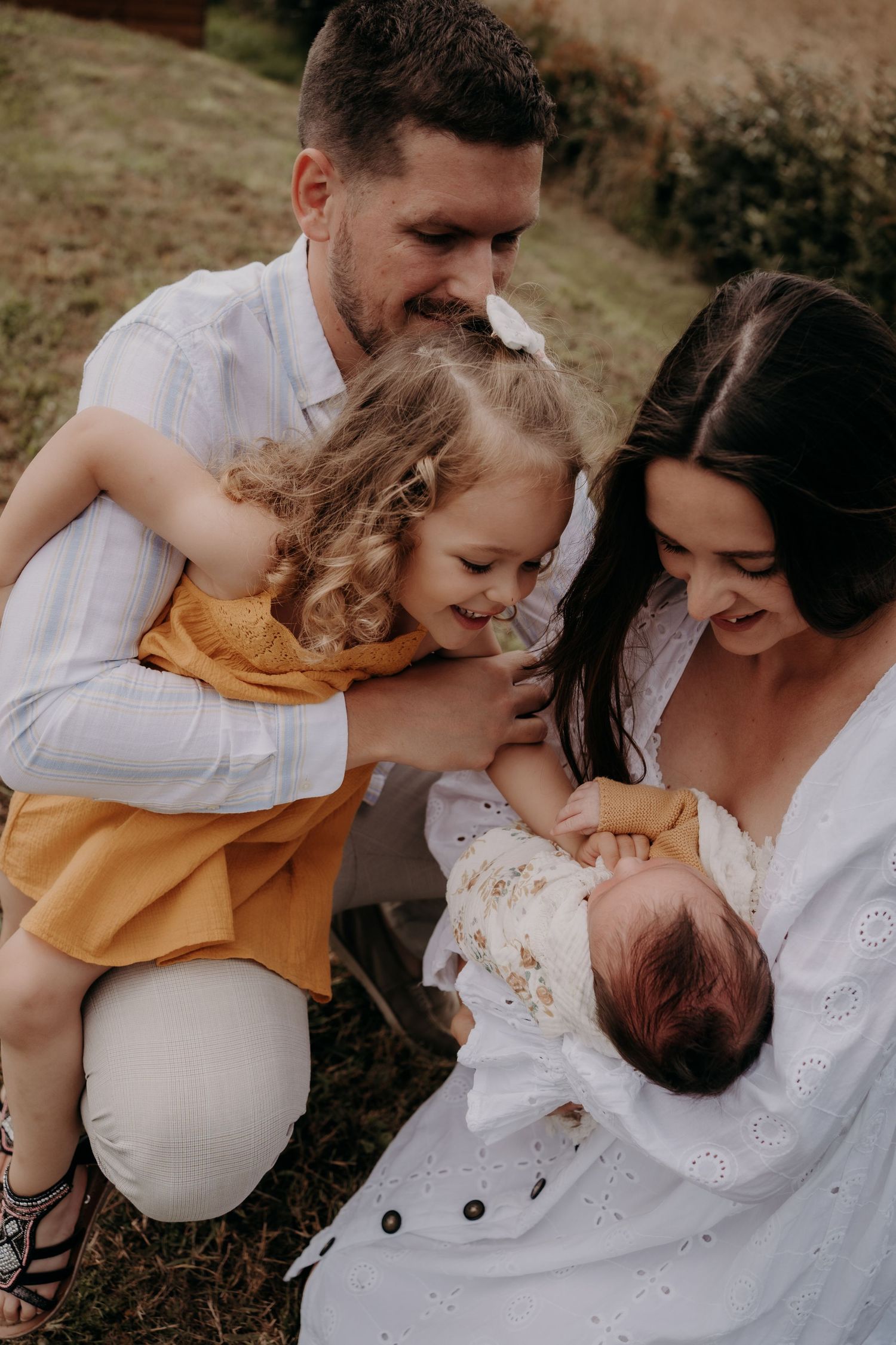 Intimate family moment as parents and child gather around newborn baby outdoors.