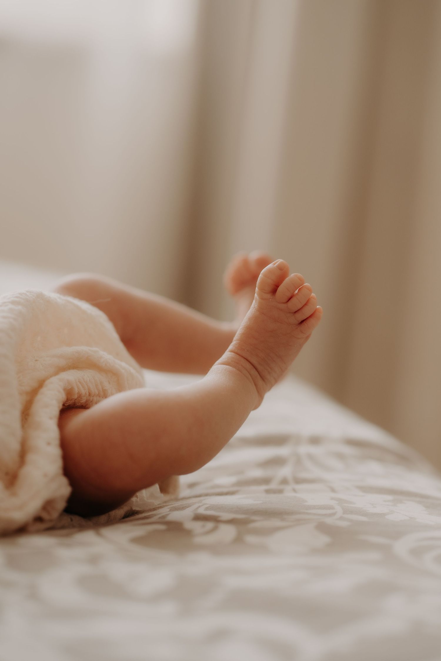 Close up of baby's foot peeking out from white blanket in soft lighting.