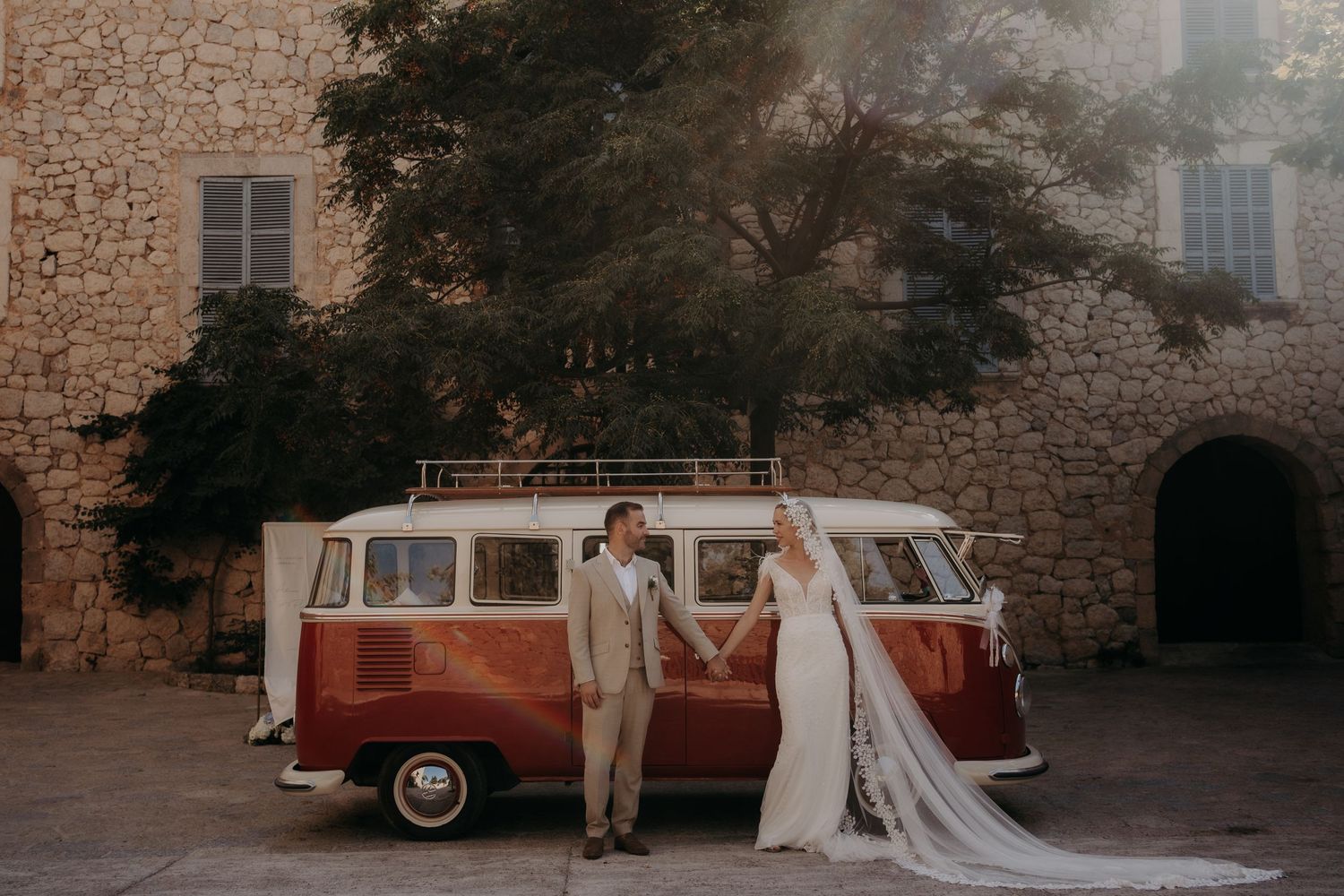 A vintage cream-colored van parked against a rustic stone wall backdrop at a wedding.