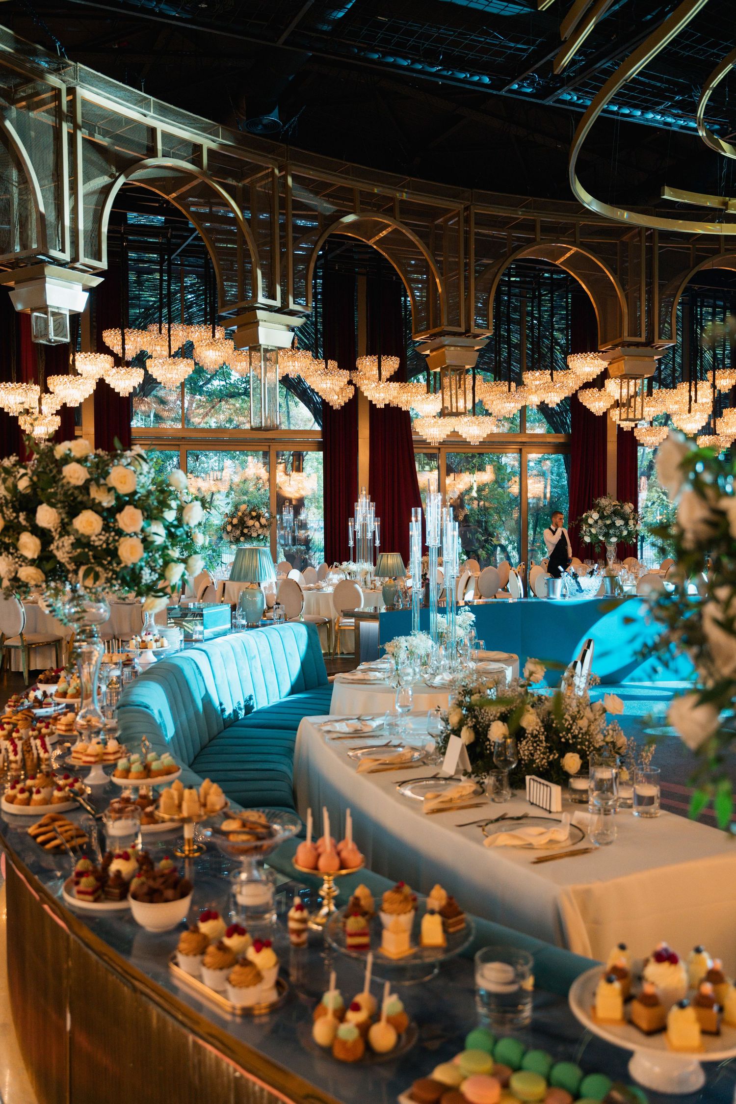 Elegant wedding reception venue with curved seating, floral centerpieces, dessert display and romantic lighting under arched ceilings.