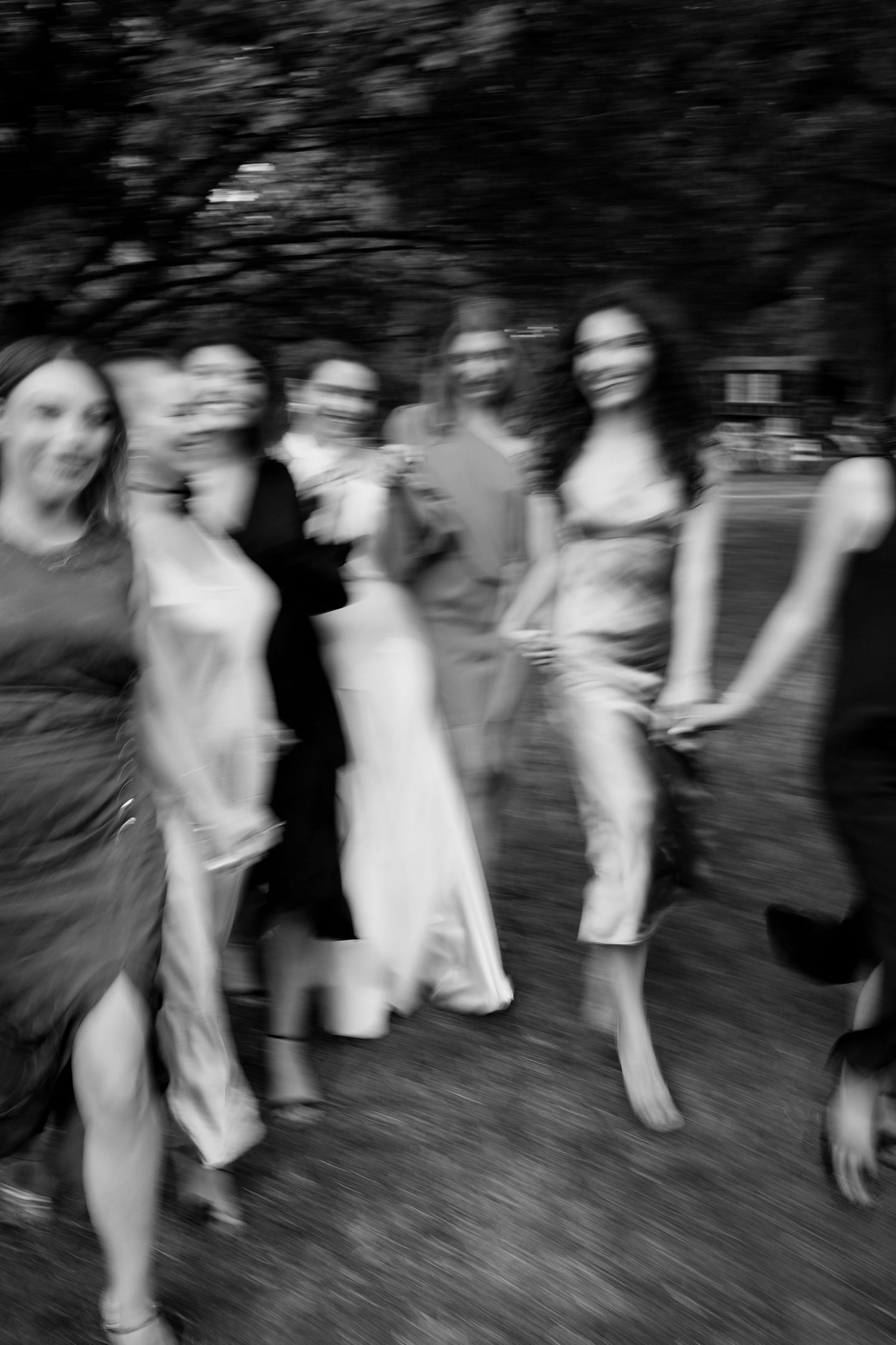 Motion-blurred black and white photo of wedding guests dancing outdoors.