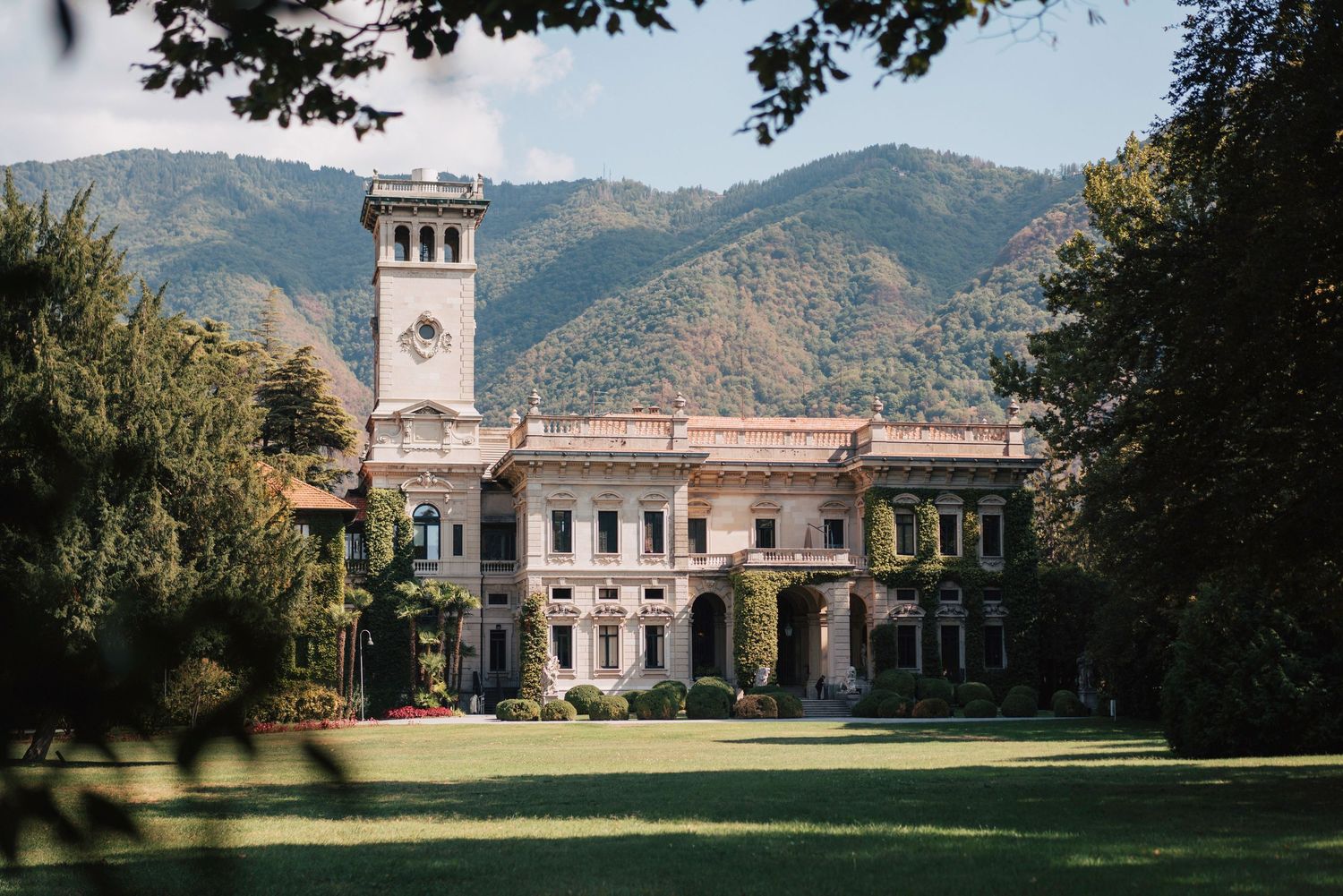 Elegant historic mansion with tower and mountain backdrop in warm sunlight.