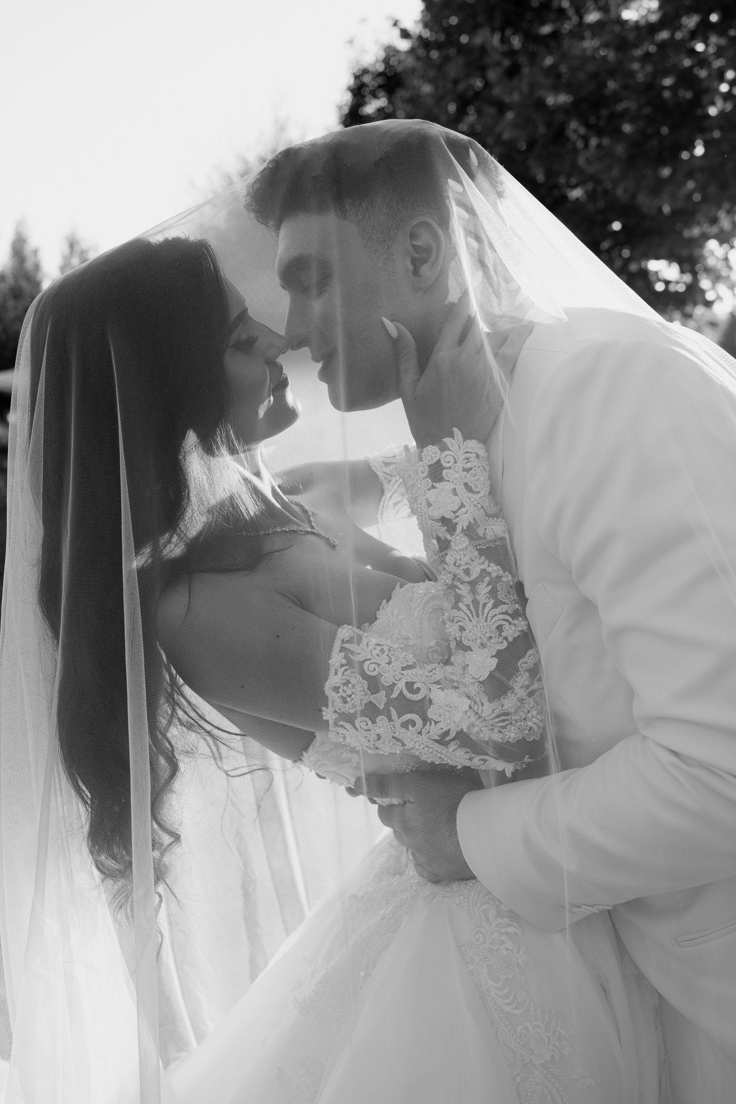 Intimate black and white portrait of newlyweds sharing tender moment under wedding veil.