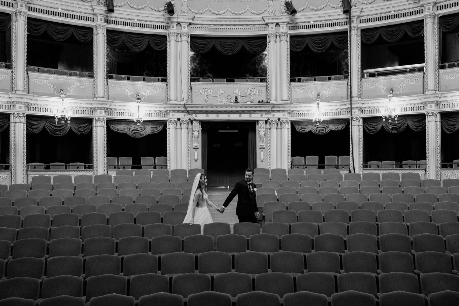 A black and white view of an empty historic theater with curved rows of seats and ornate balcony levels.
