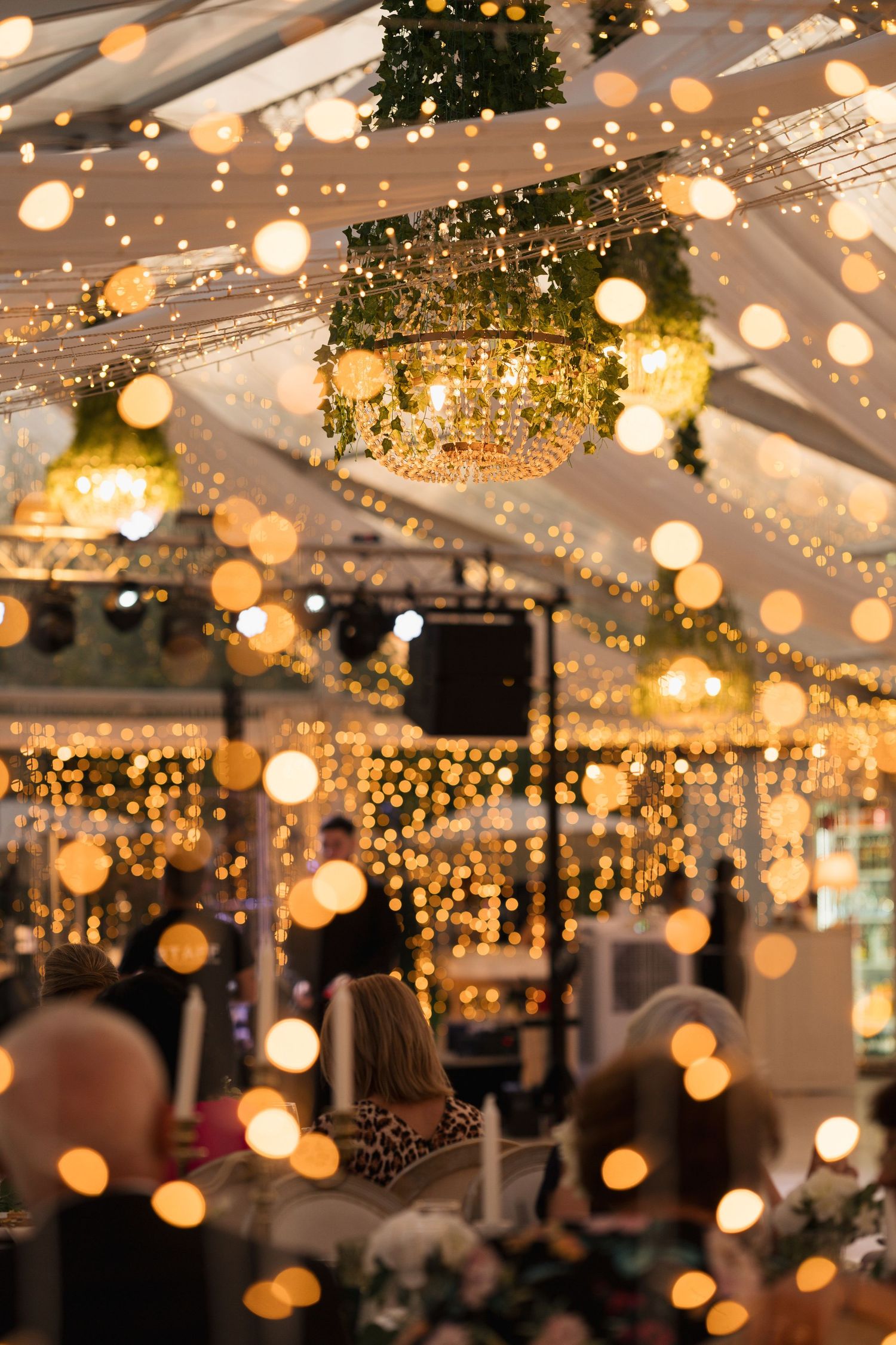 Warm string lights and bokeh create a magical ambiance at an evening wedding reception under a tent canopy.