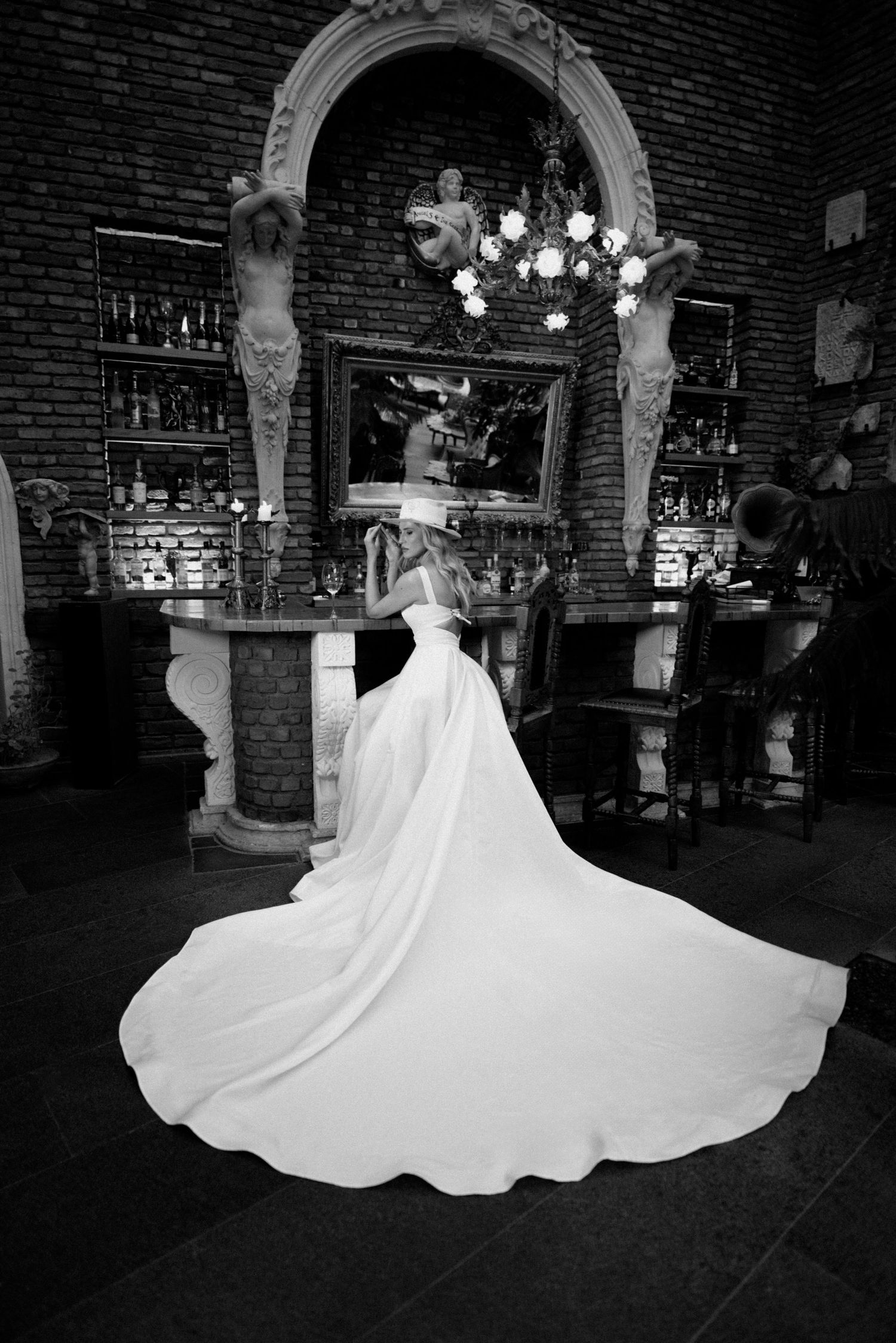 A series of black and white photos showing a white wedding dress twirling in an elegant brick-walled venue with chandeliers.