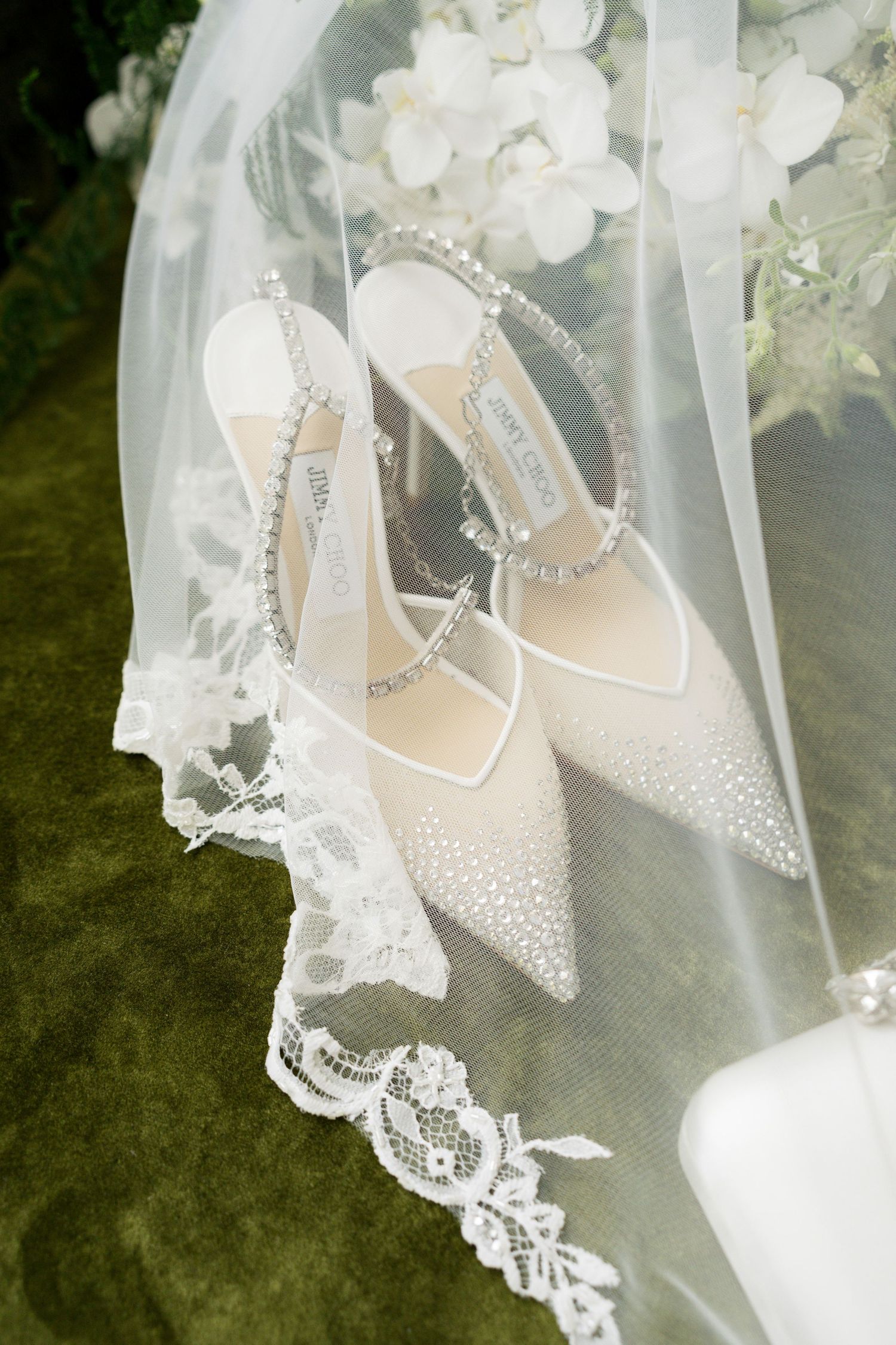 Delicate bridal shoes with crystal details and lace veil details in soft focus.