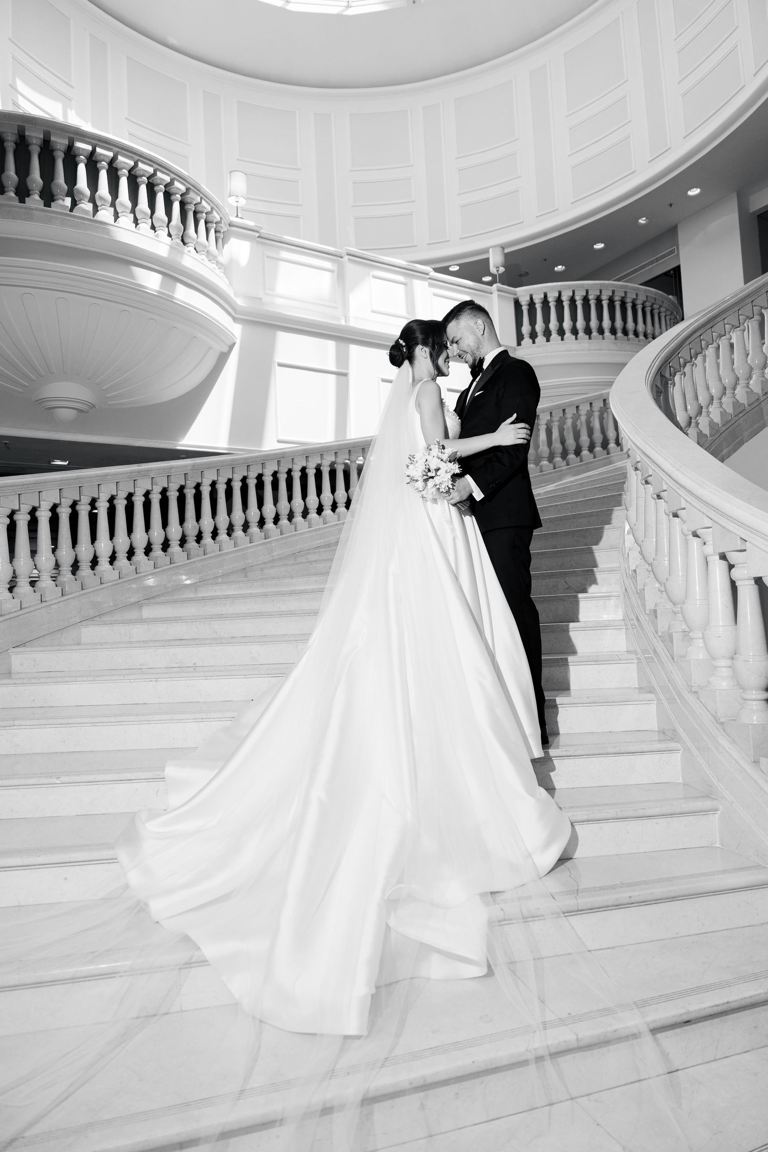 Elegant black and white wedding photos on grand marble staircase showing romantic poses and flowing white dress.