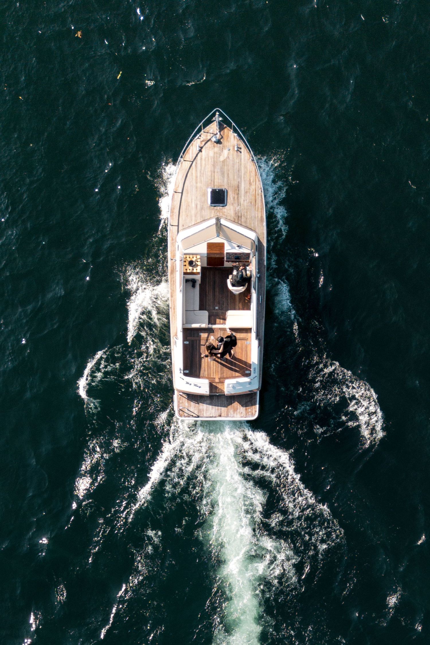 Aerial view of a luxury motorboat speeding through dark green ocean waters, leaving a white wake trail.