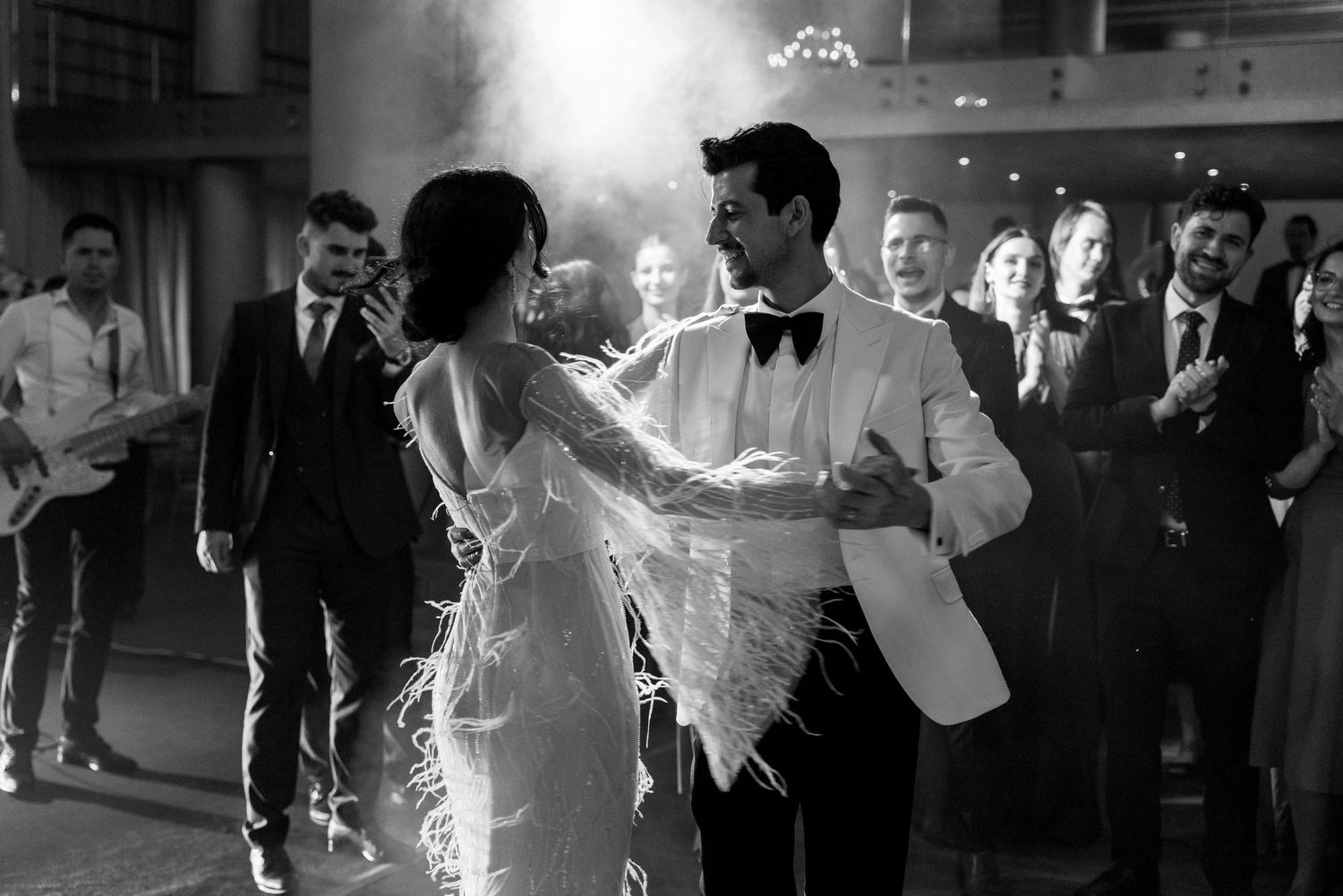 Black and white photo of couple dancing at wedding reception with guests watching.
