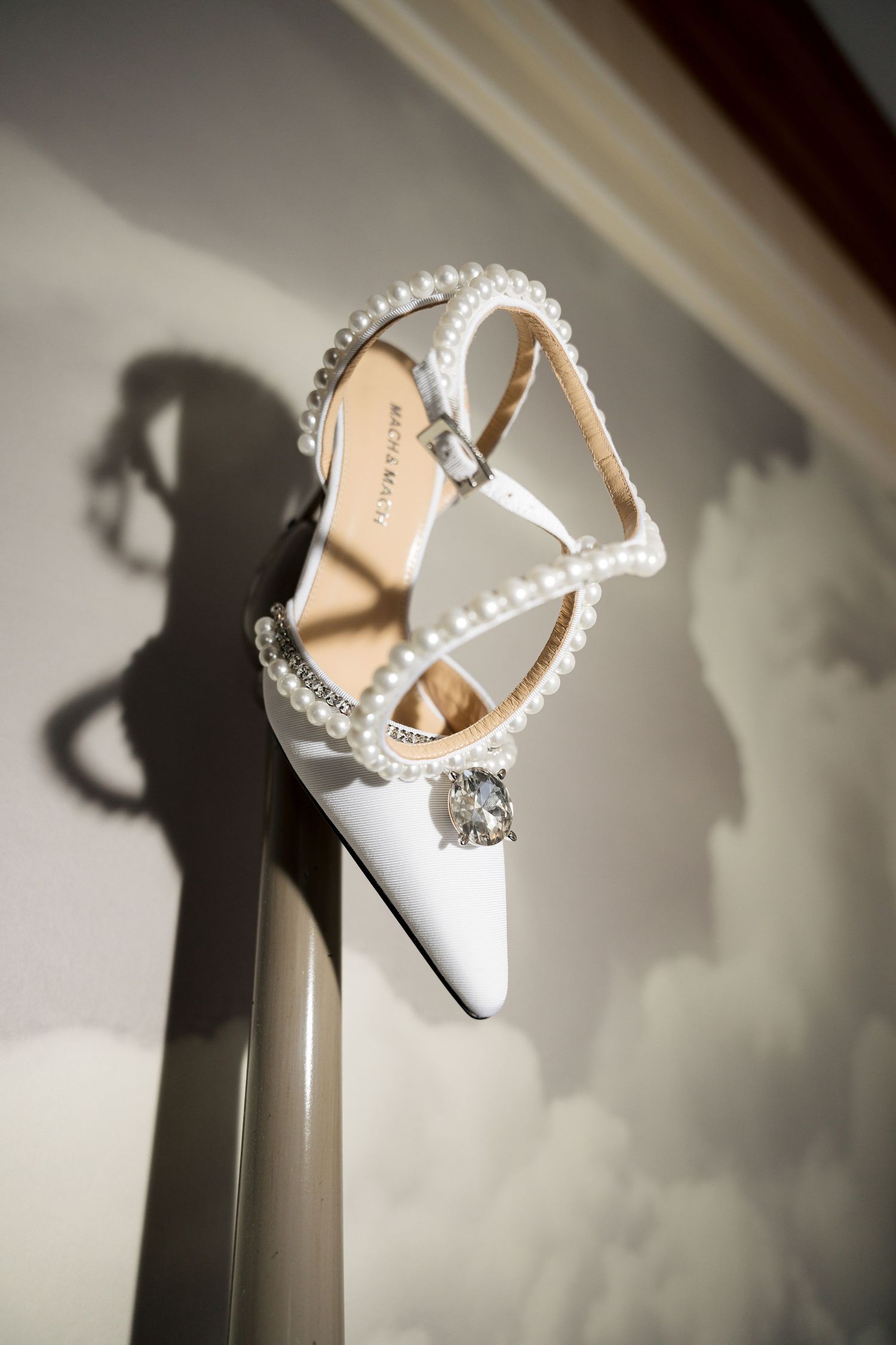 White bridal shoes with pearl straps casting dramatic shadows against light background.
