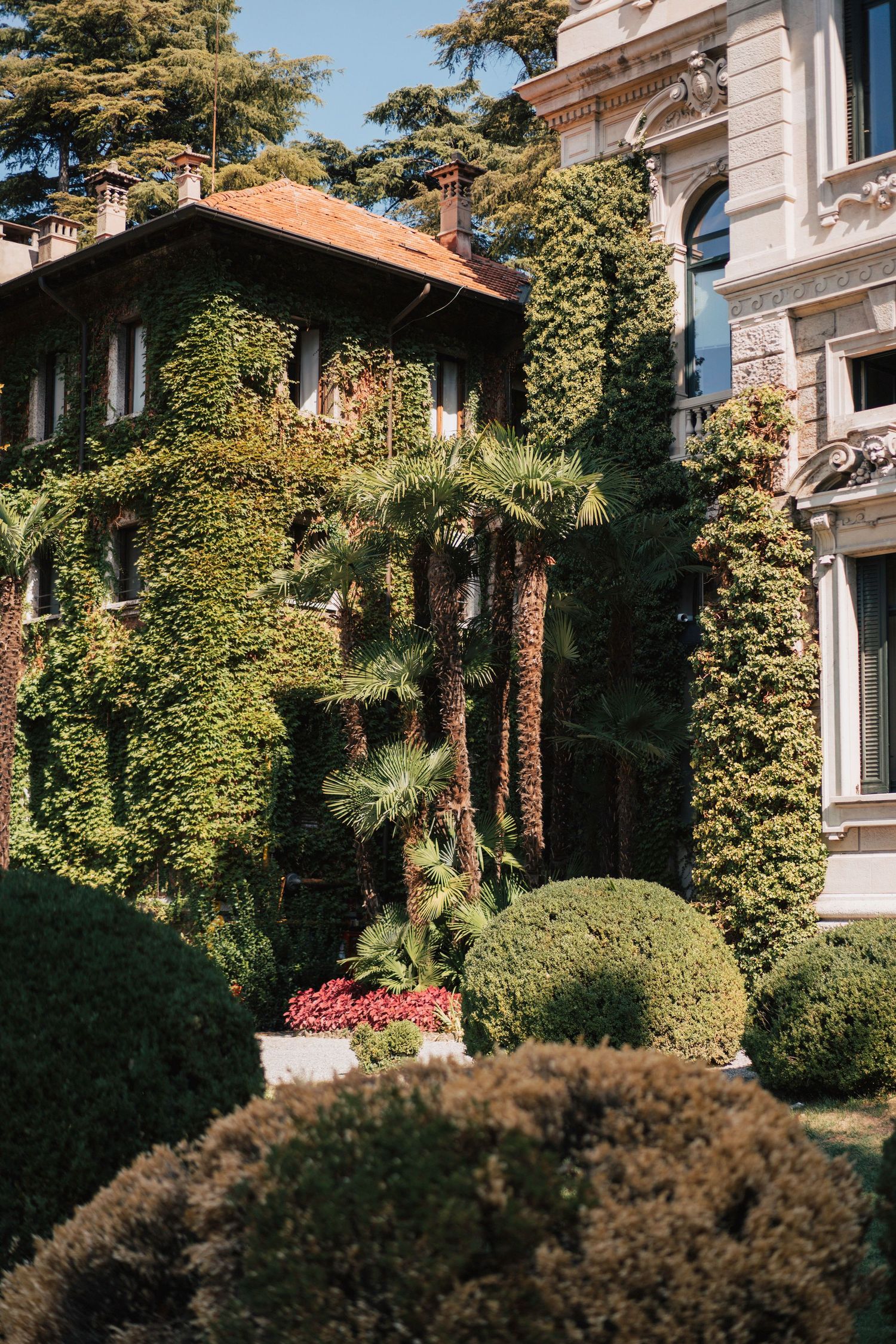 Lush garden view with tall trees and classic architecture featuring ornate white building details and terracotta roofing.