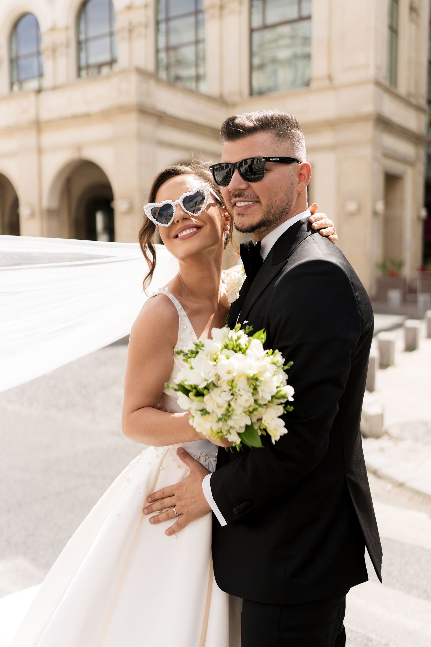 Romantic wedding portraits with couple wearing sunglasses and holding white bouquet in bright sunlight.
