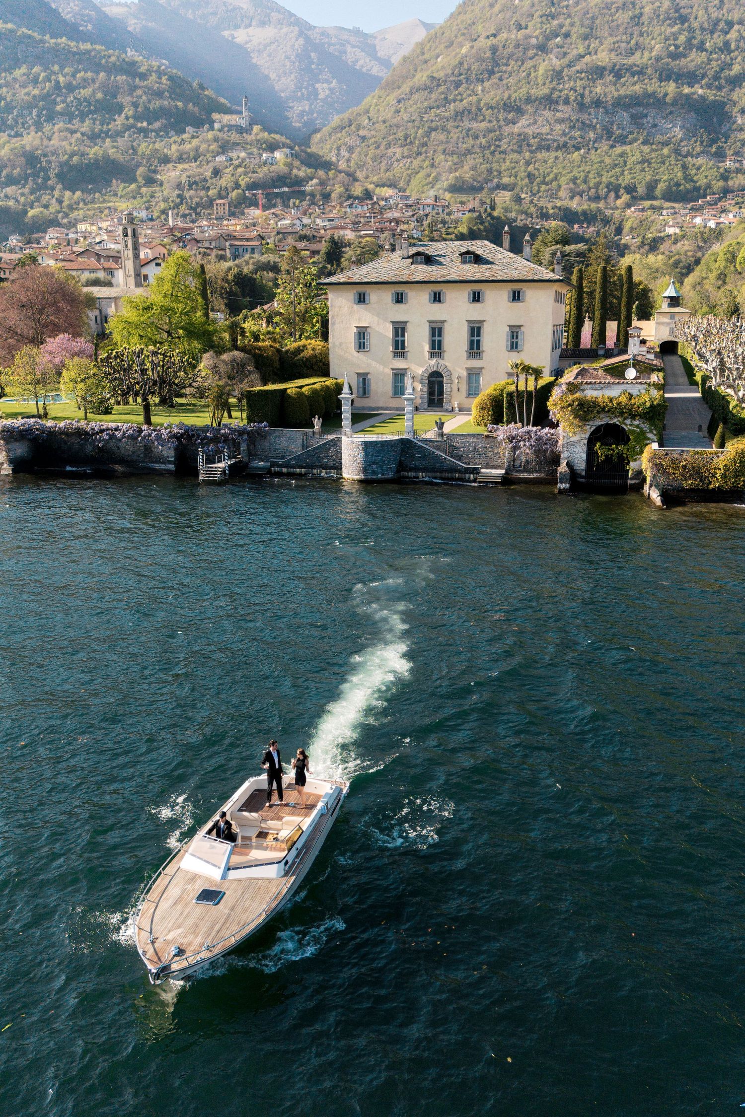 Aerial view of a luxury speedboat on Lake Como with an elegant Italian villa and lush green mountains in the background.