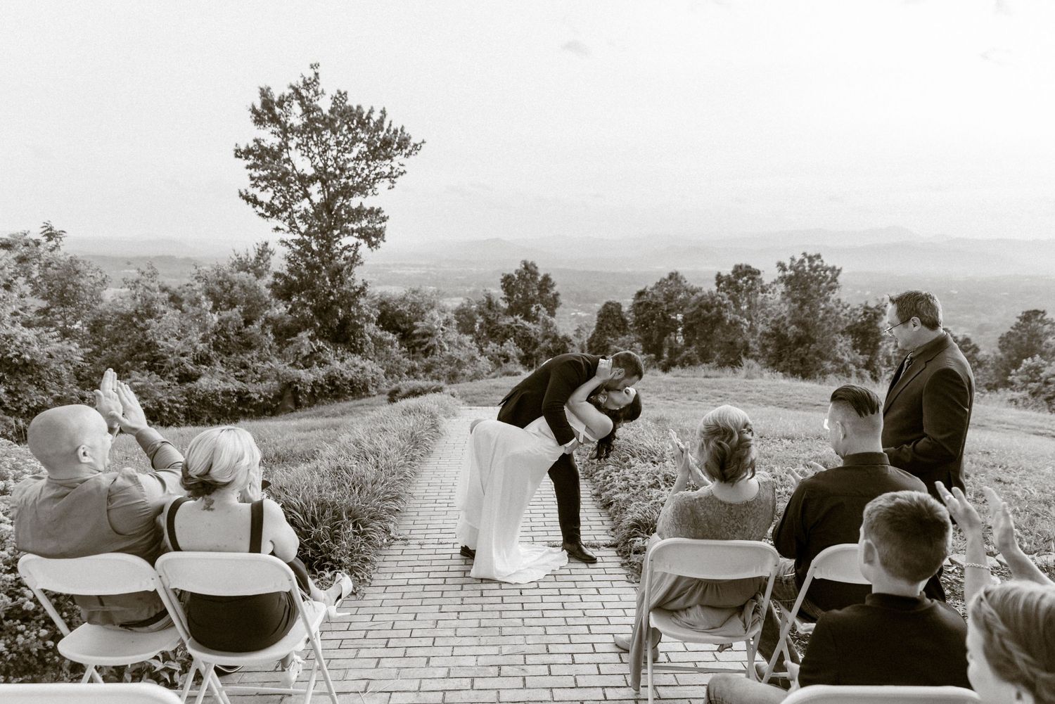 Newly married couple sharing a joyful kiss surrounded by family and friends.