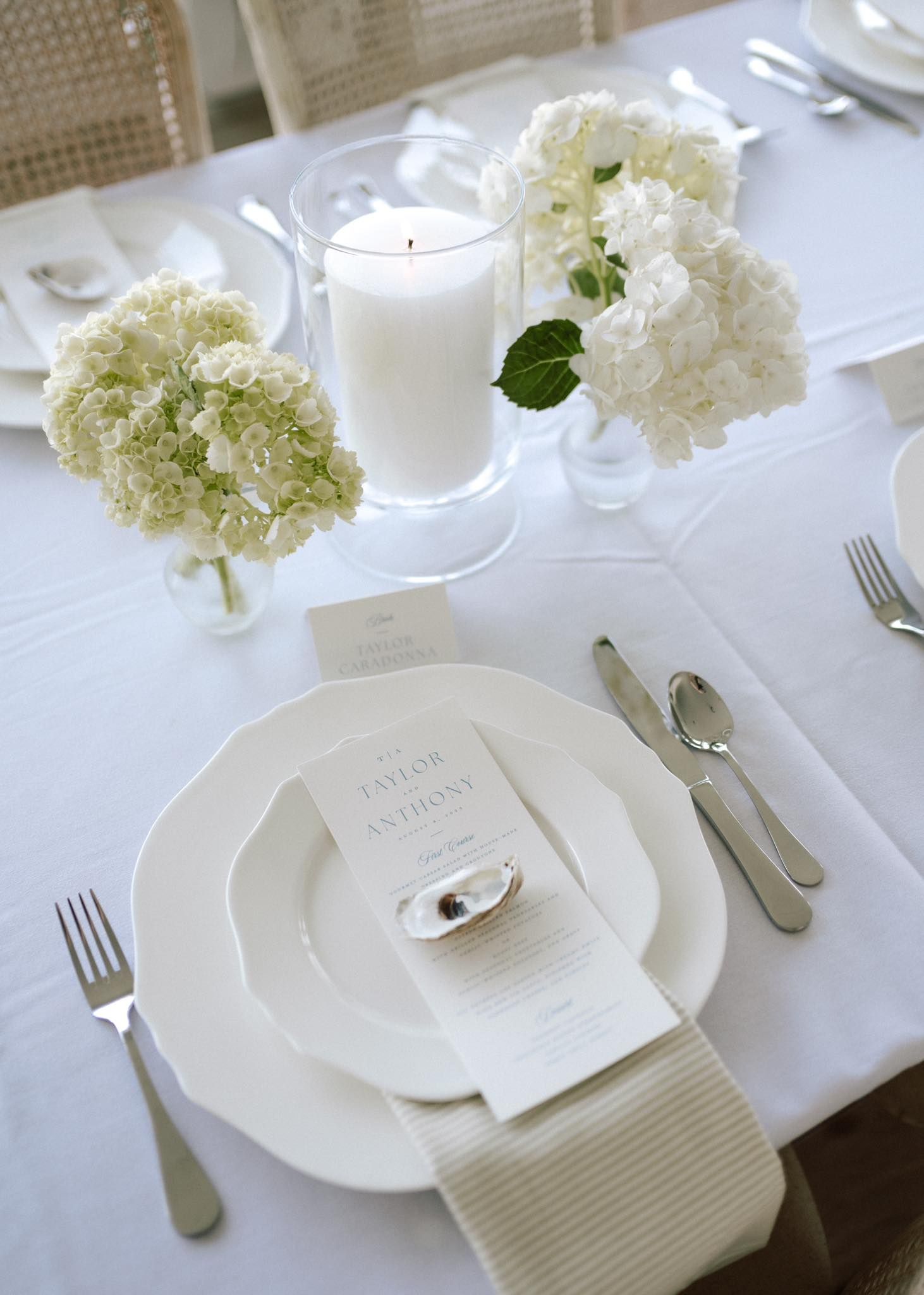Close-up of wedding place setting with menu card, oyster shell, linen napkin, and flatware.