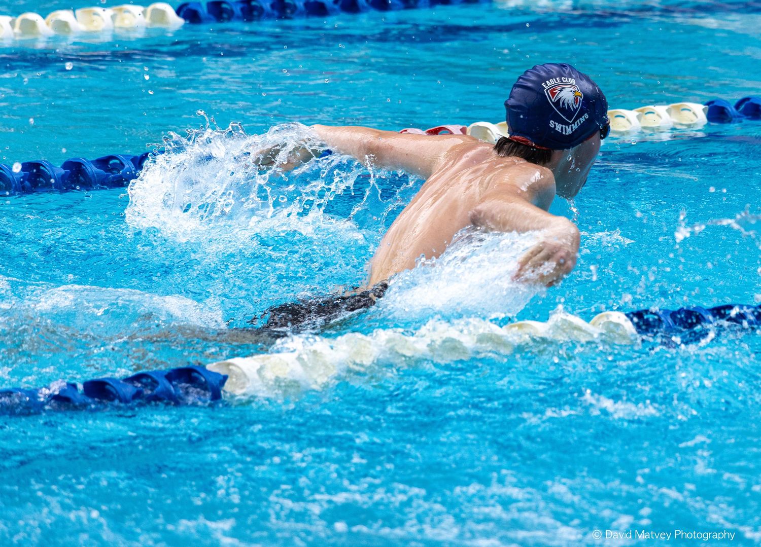 Competitive swimmer performing butterfly stroke in a bright blue outdoor pool.