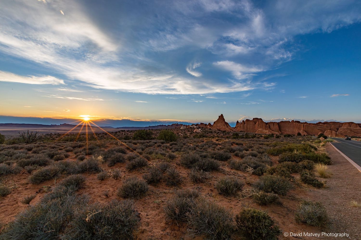 Desert landscape at sunrise with red rock formations and road at Arches National Park.