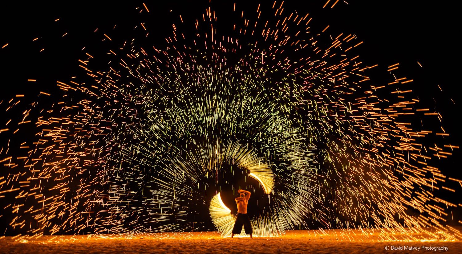 Person spinning glowing steel wool creating fiery light trails at night.
