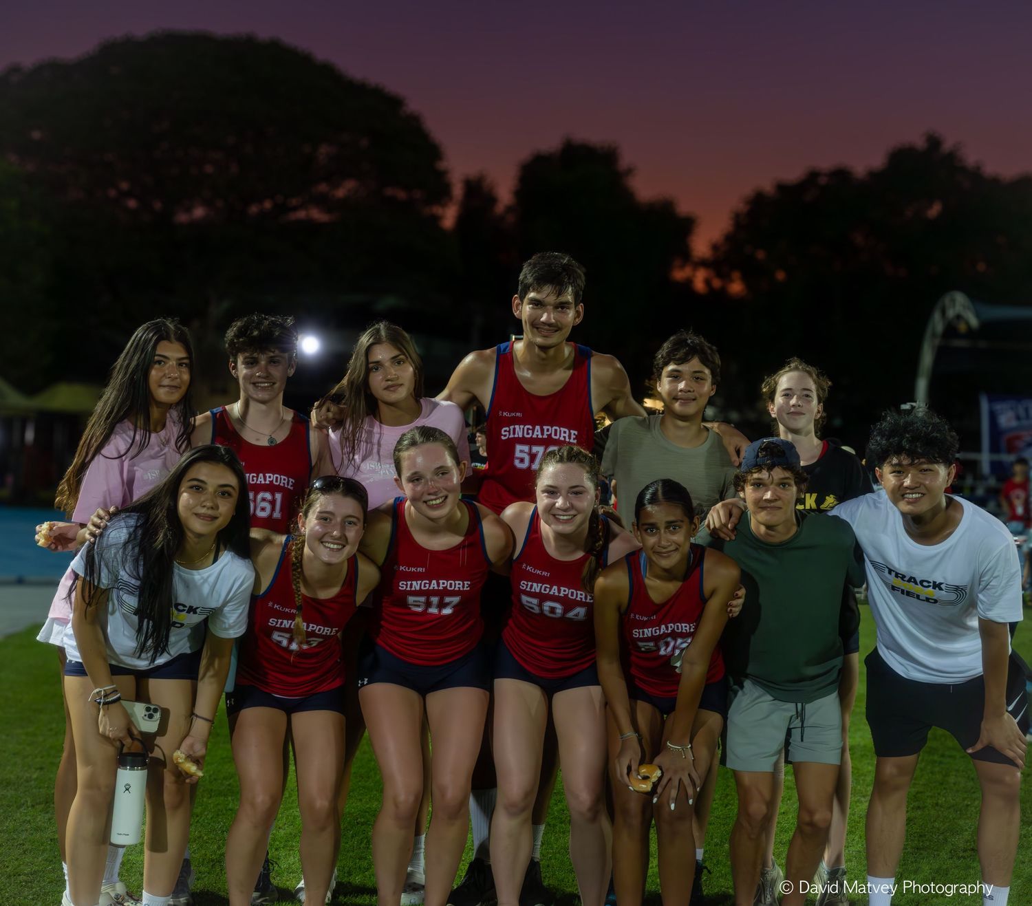 Group of Singapore American School track and field athletes posing at sunset.