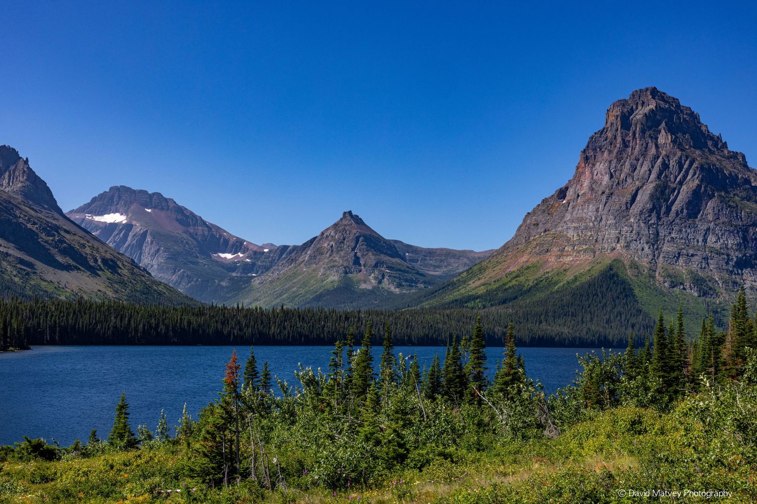 Stunning alpine lake surrounded by evergreen forests and jagged mountain peaks in Glacier National Park.