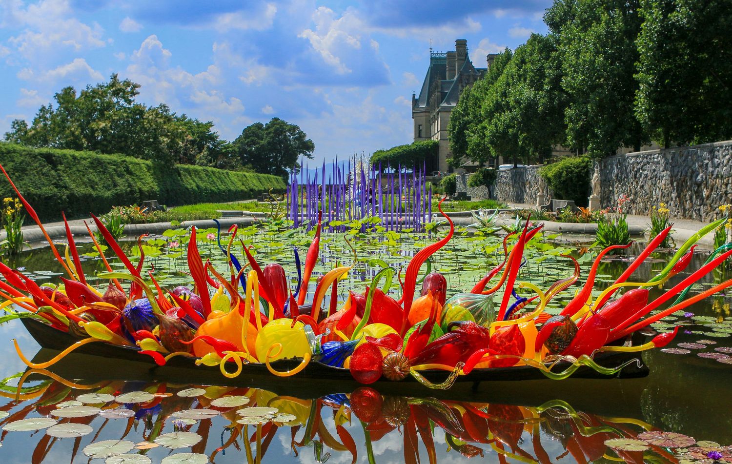 Colorful Chihuly glass sculpture floating in lily pond with lush garden and estate backdrop.