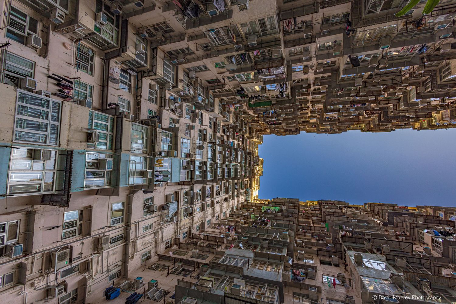Dramatic upward view of densely packed apartment buildings surrounding a narrow sky opening in Hong Kong.