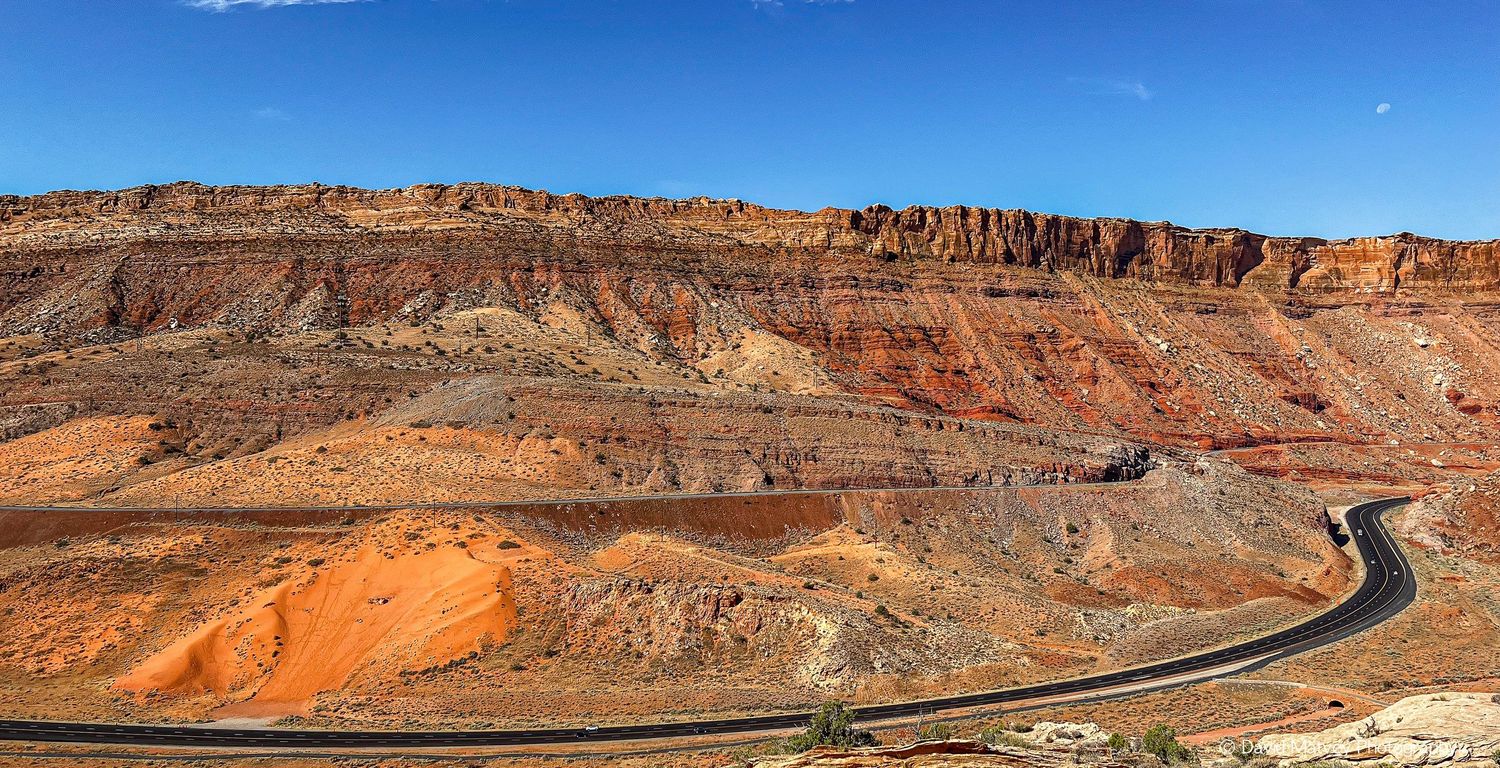 Scenic highway curving through colorful stratified red rock canyon cliffs under blue sky.