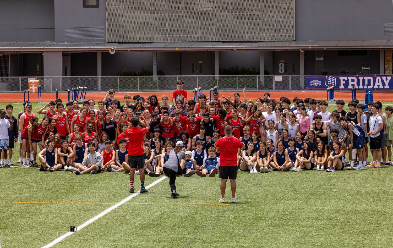 Large group of students and coaches posing on sports field during school event.