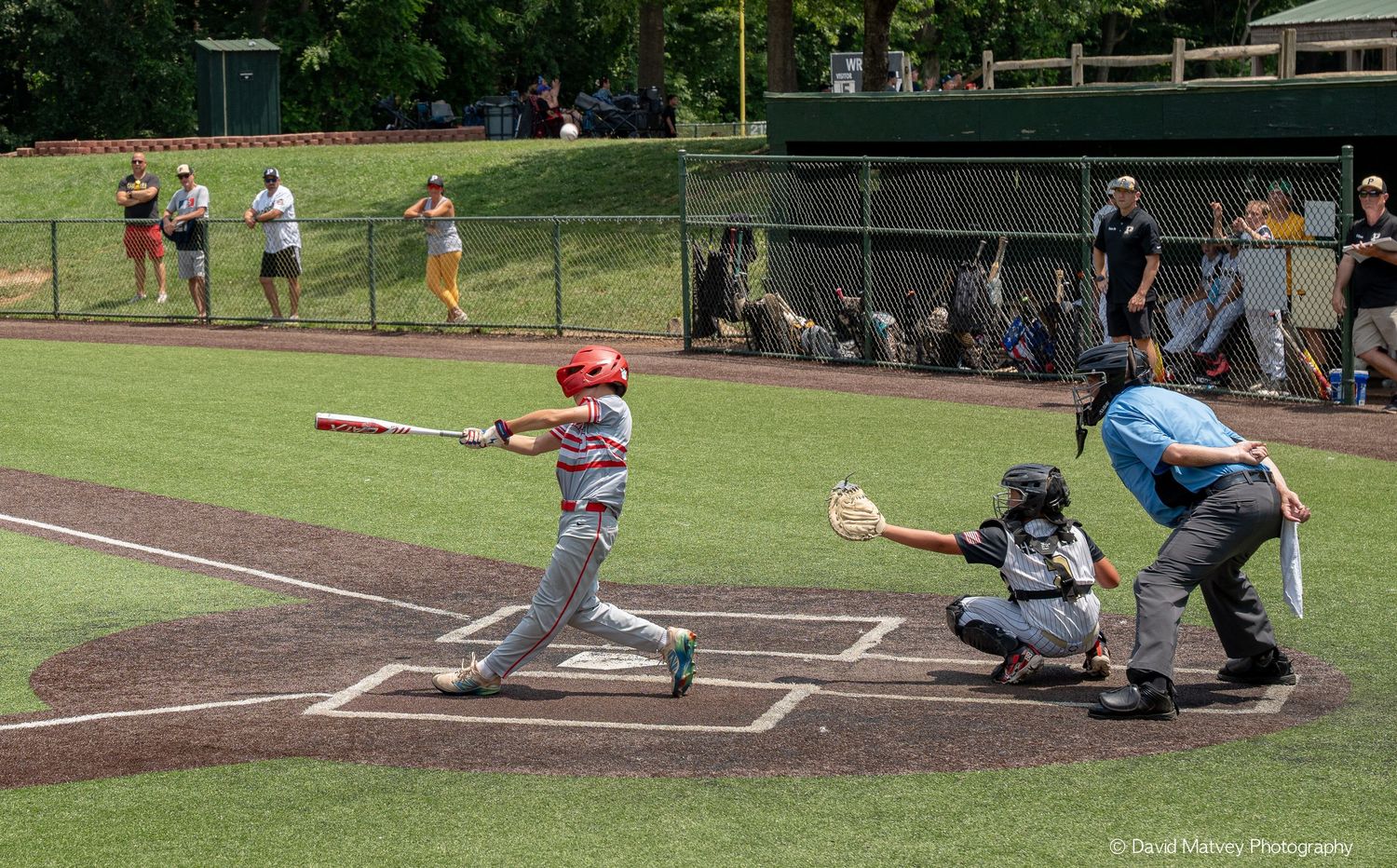 Young baseball batter swings at pitch with catcher and umpire during youth league game.