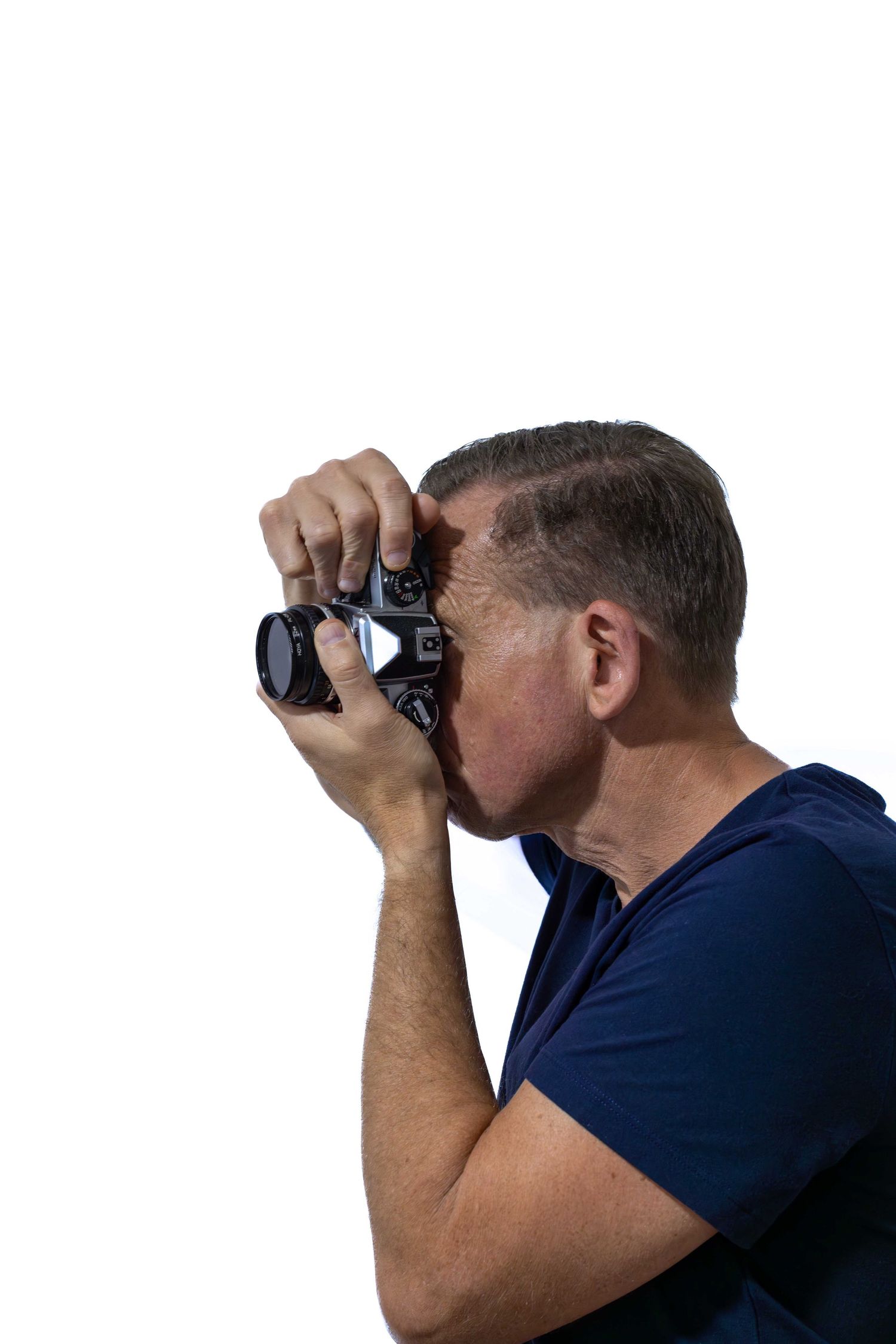 Middle-aged man in blue t-shirt photographing with DSLR camera on white background.