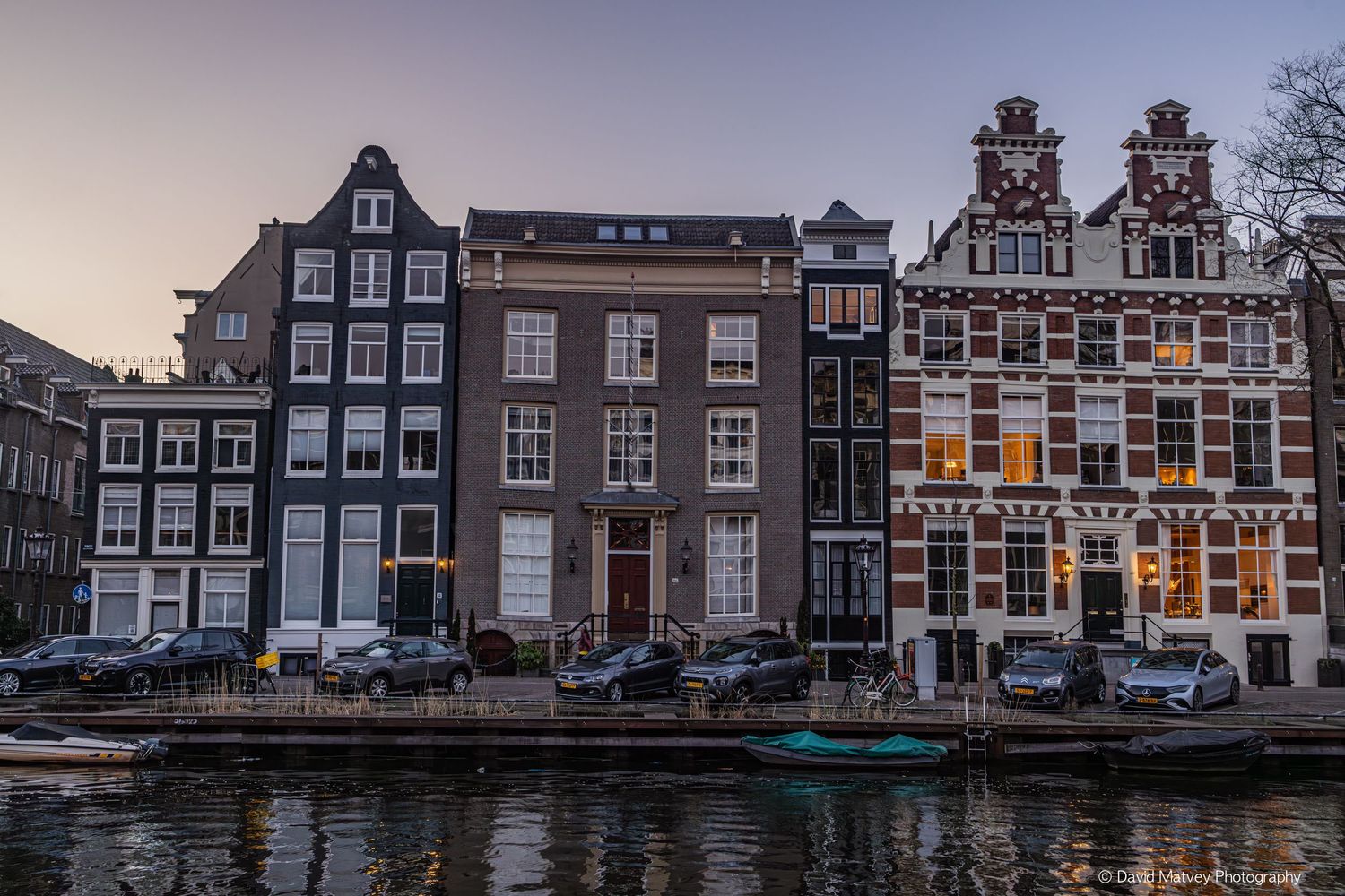 Historic Amsterdam canal houses with stepped gable rooftops reflected in still water at dusk.